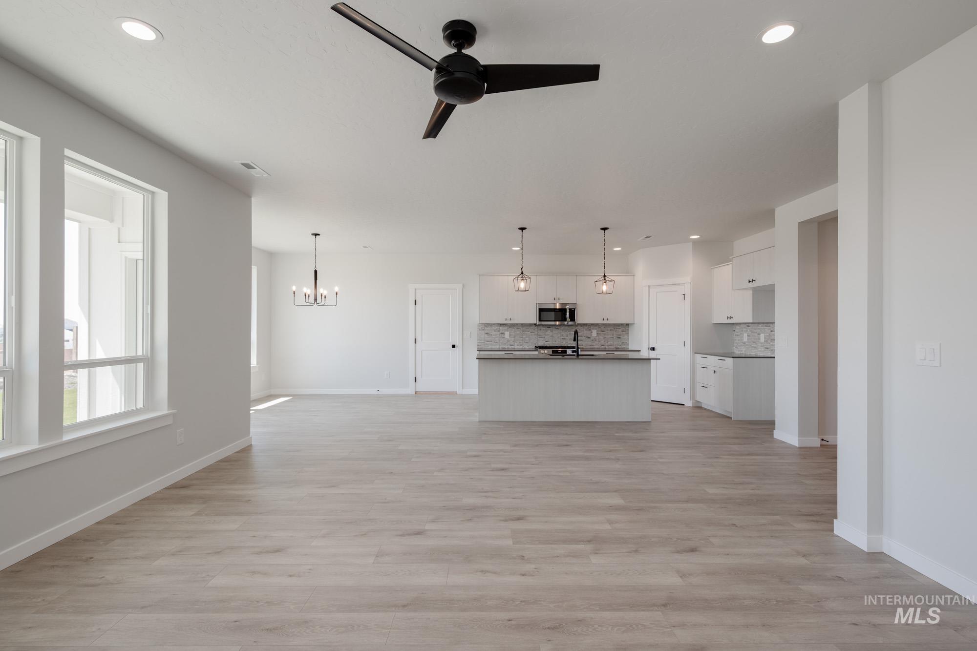 Unfurnished living room featuring recessed lighting, a ceiling fan, a chandelier, and light wood-style flooring