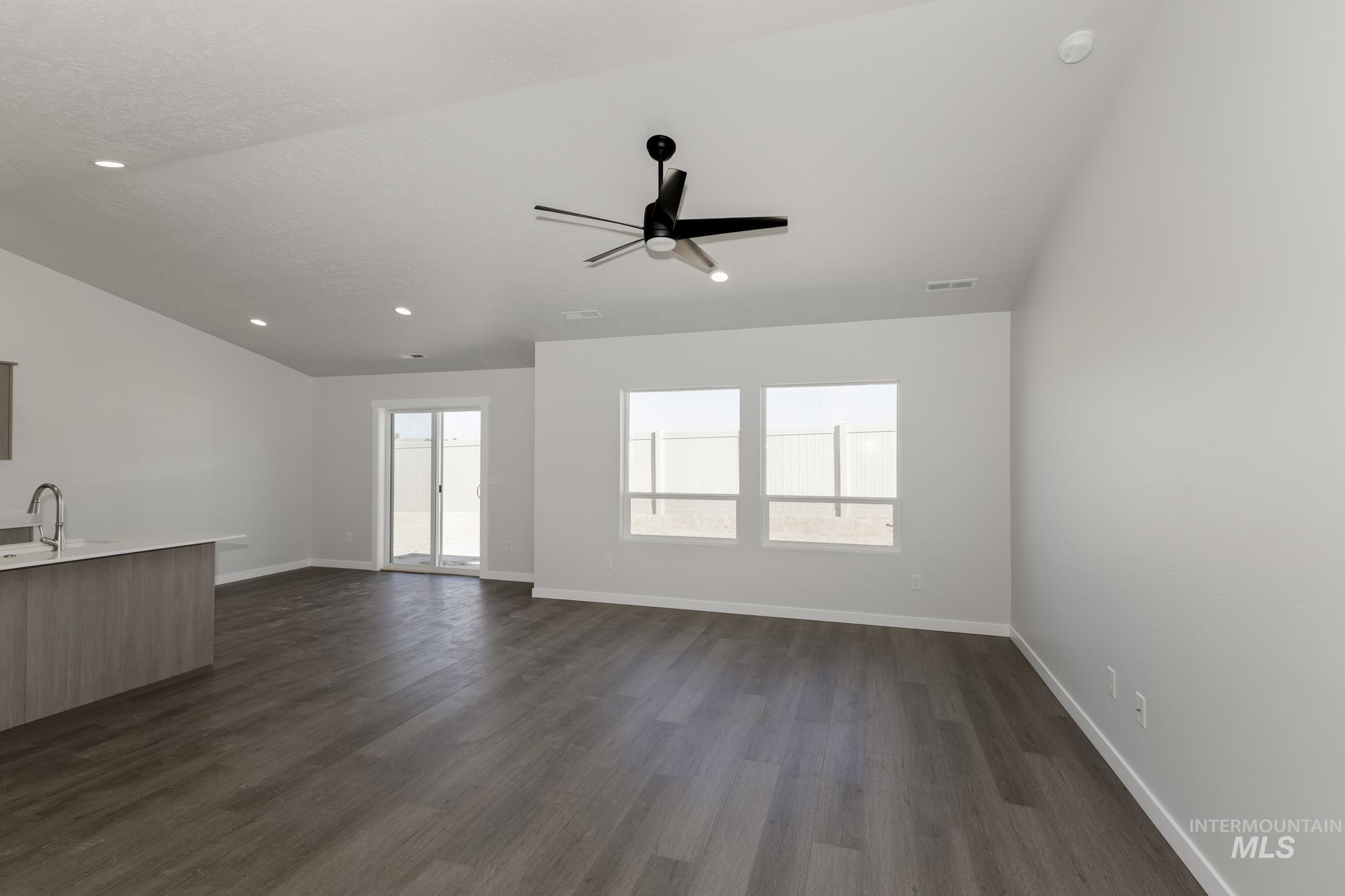 Unfurnished living room featuring plenty of natural light, dark wood-type flooring, a ceiling fan, vaulted ceiling, and recessed lighting