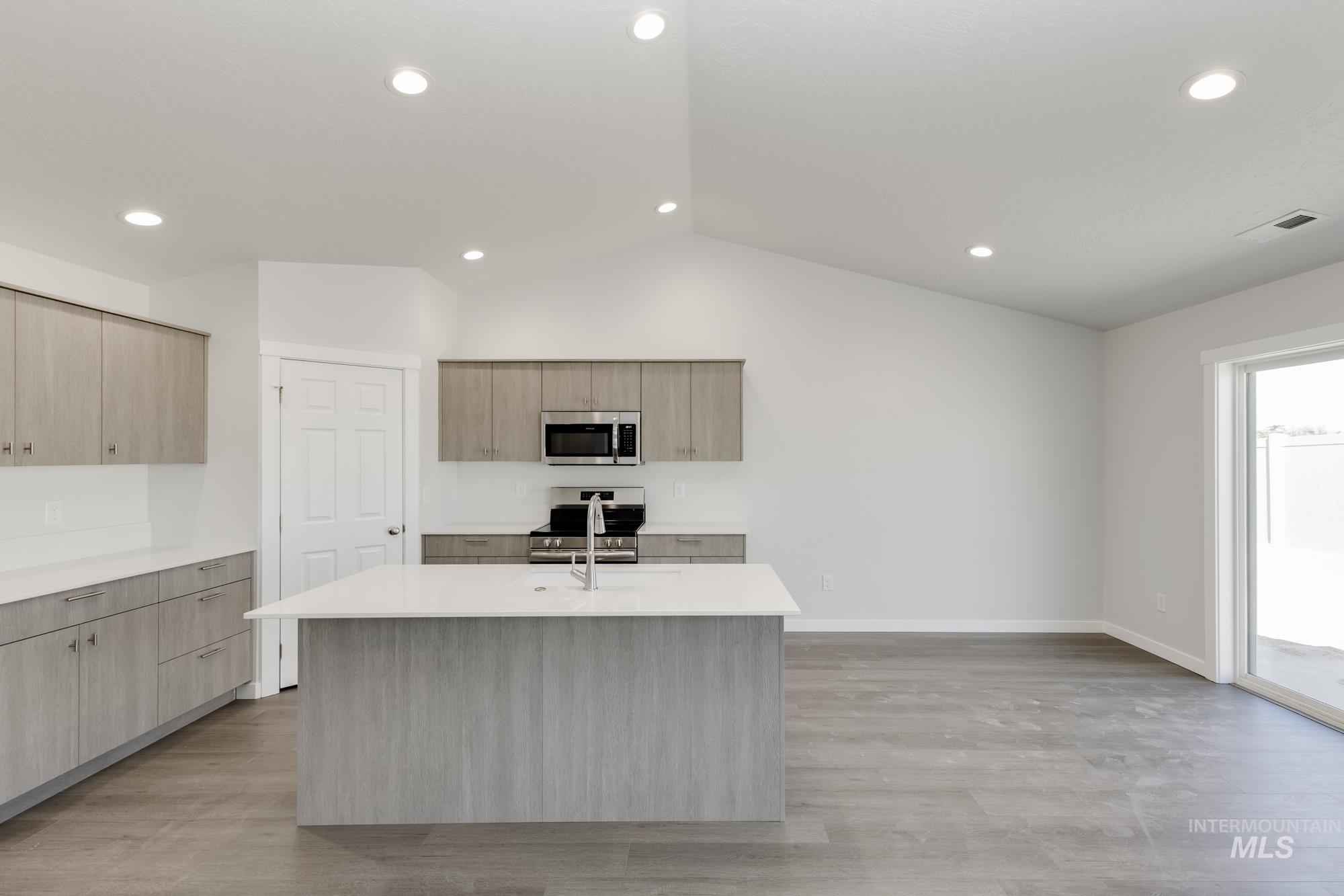 Kitchen with lofted ceiling, light stone counters, a center island with sink, appliances with stainless steel finishes, and light wood-type flooring