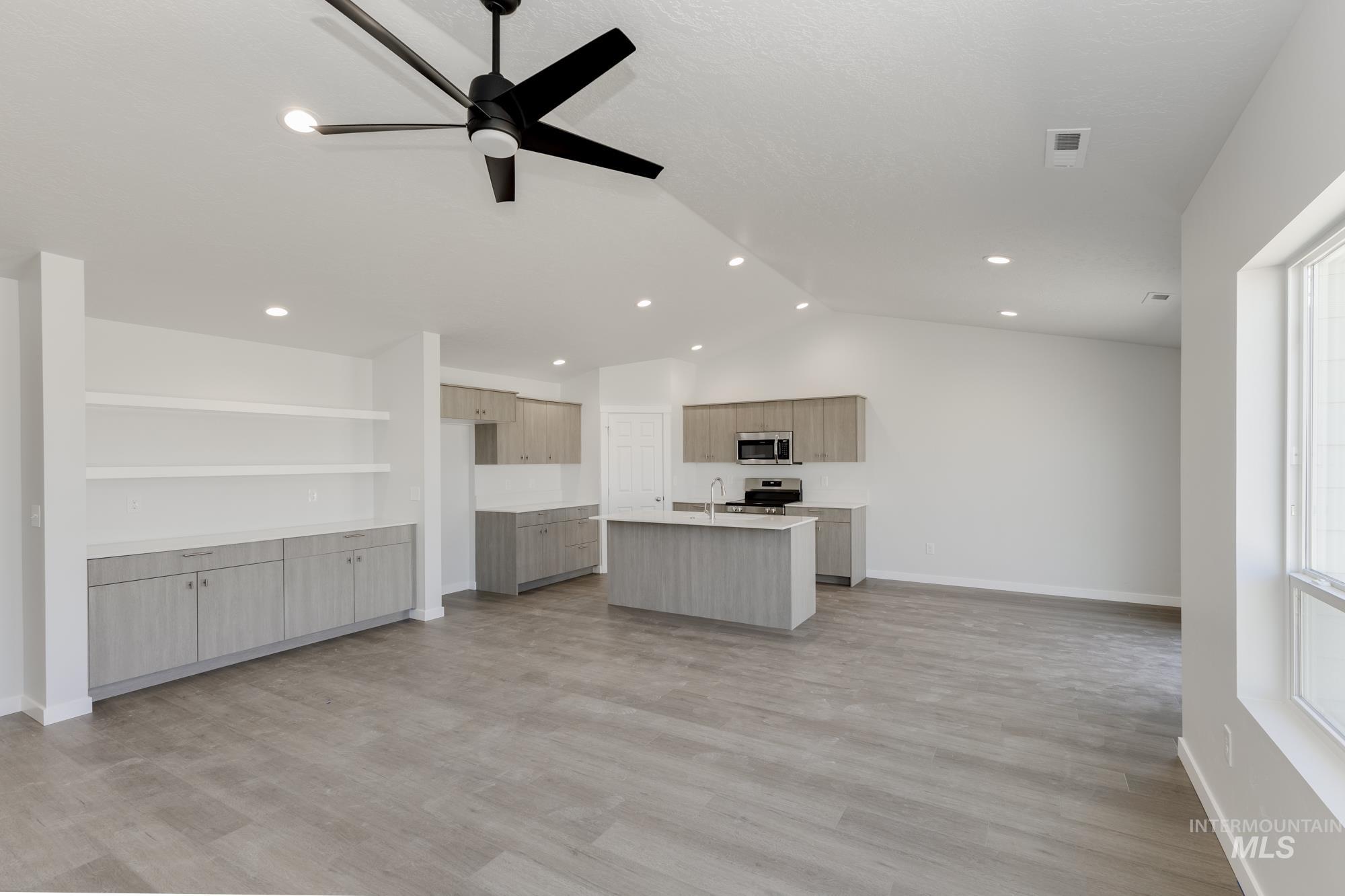 Kitchen with open floor plan, light countertops, vaulted ceiling, an island with sink, and light wood finished floors