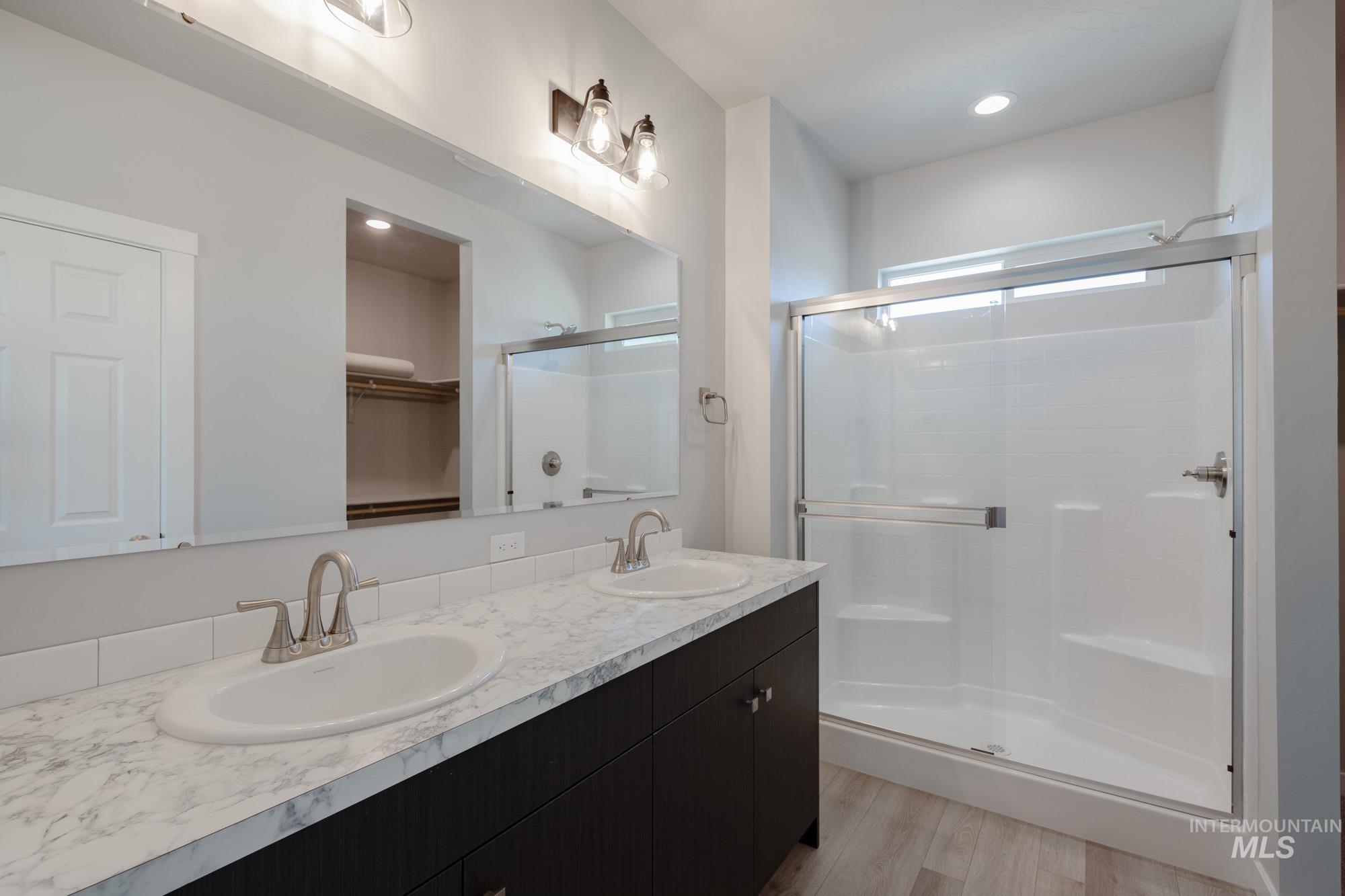 Bathroom with a spacious closet, light wood finished floors, double vanity, a shower stall, and recessed lighting