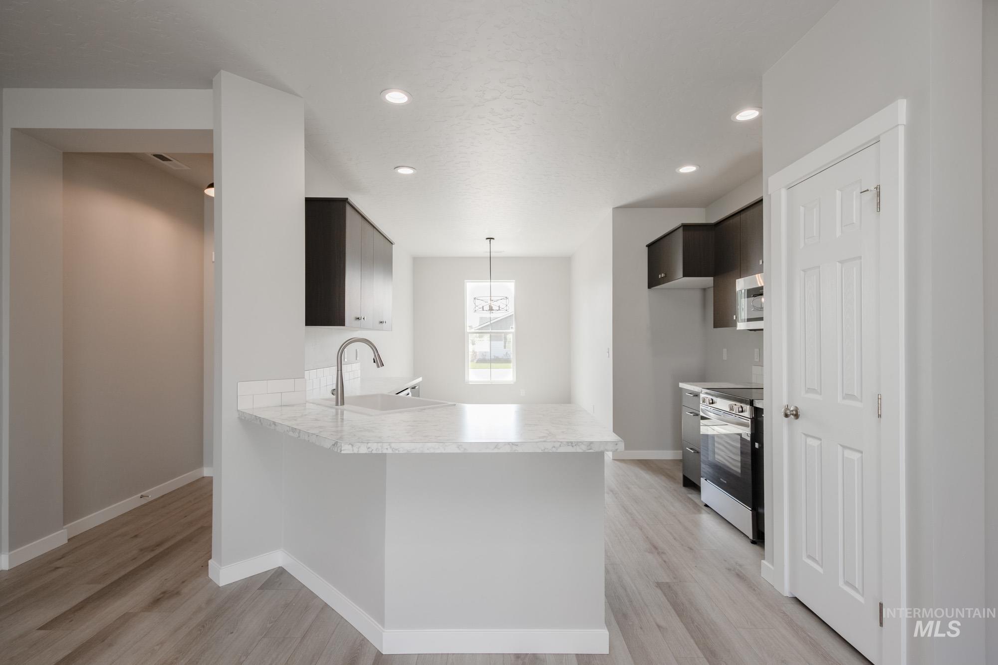 Kitchen featuring light countertops, recessed lighting, light wood-type flooring, stainless steel appliances, and a peninsula