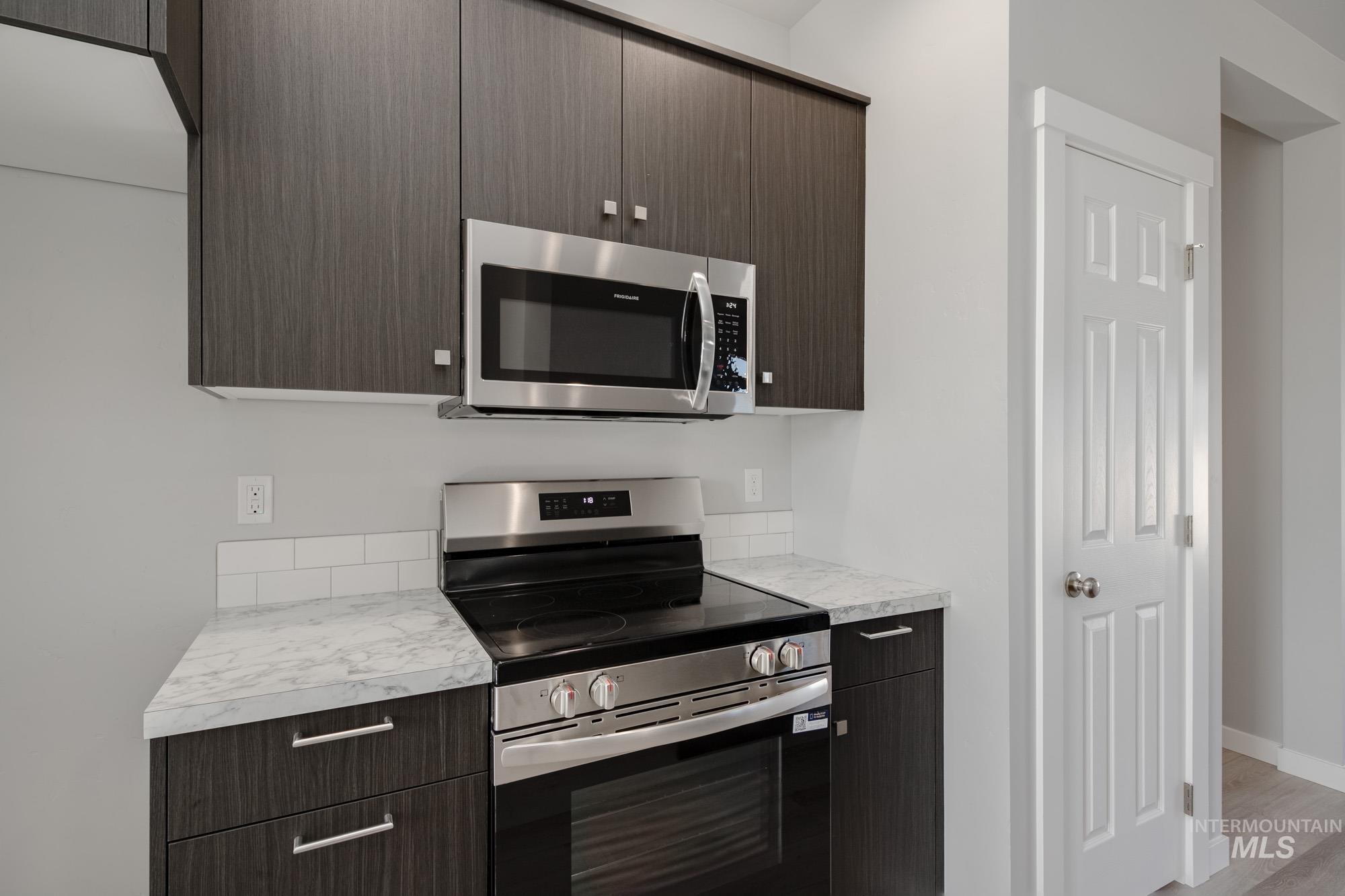 Kitchen featuring appliances with stainless steel finishes, light countertops, dark brown cabinets, modern cabinets, and light wood-style floors