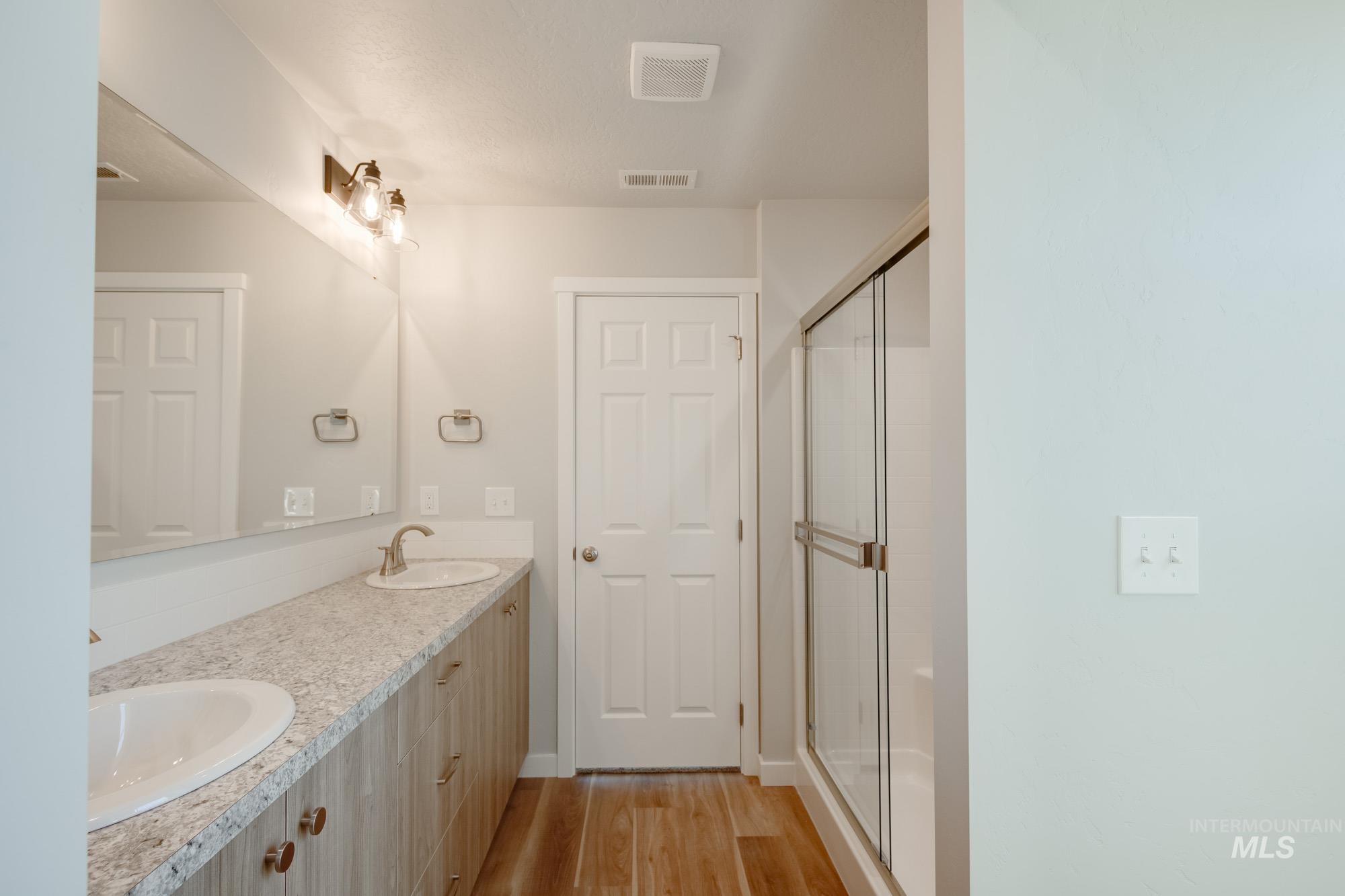 Bathroom with light wood-type flooring, double vanity, and a shower stall
