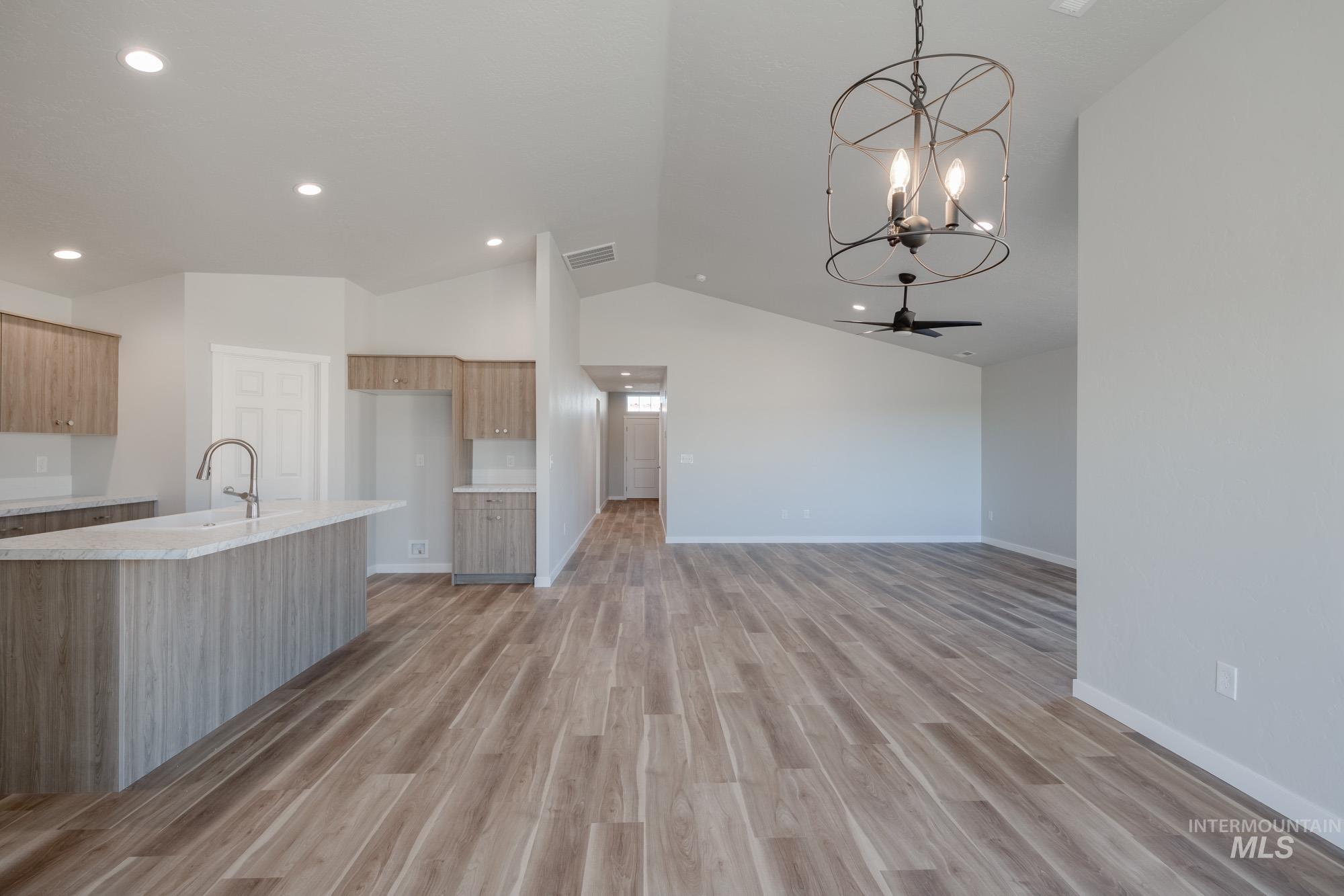 Kitchen with vaulted ceiling, pendant lighting, an island with sink, light wood-style flooring, and a chandelier
