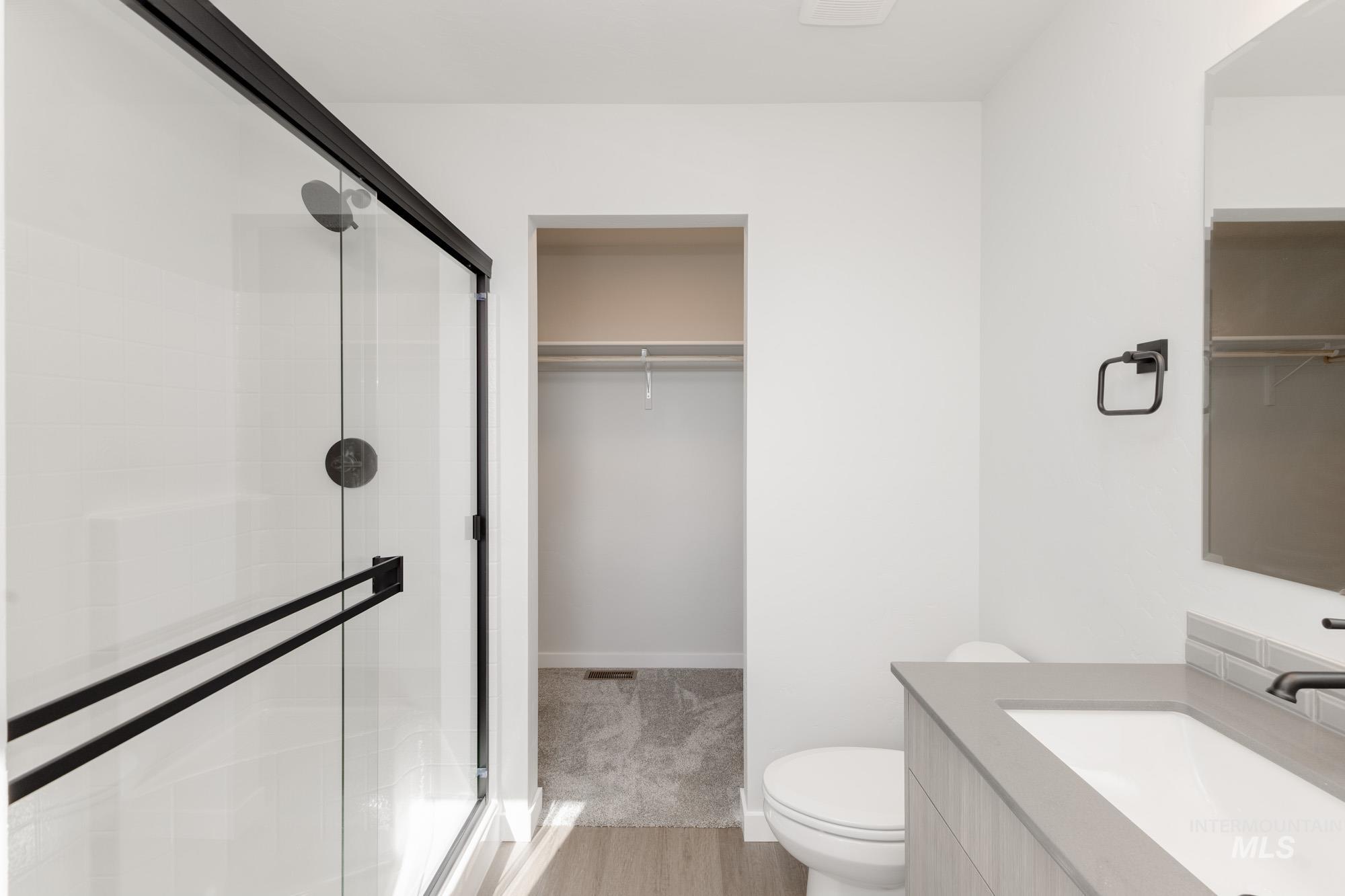 Full bath featuring a spacious closet, a stall shower, vanity, and light wood-style flooring