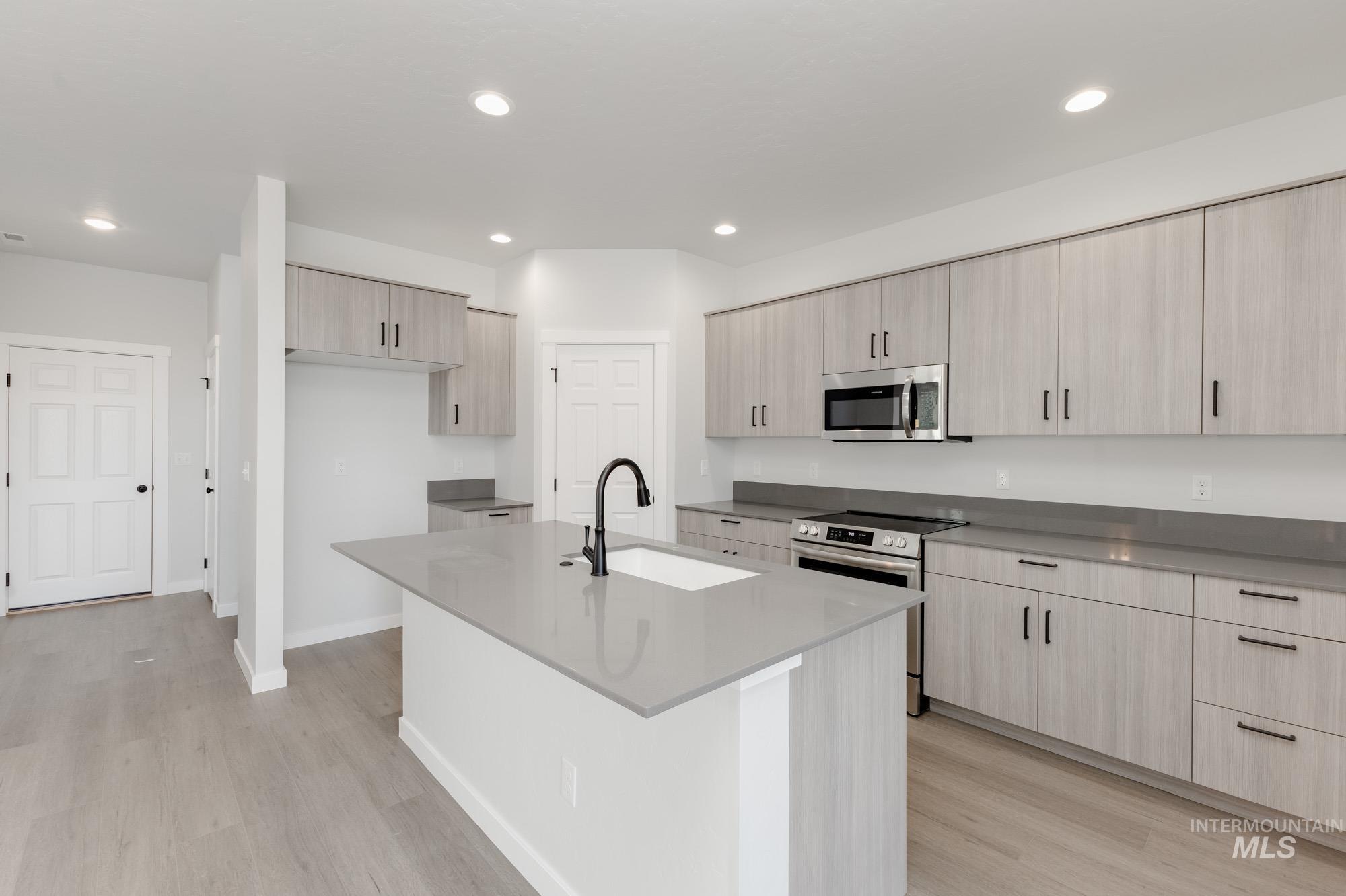 Kitchen with appliances with stainless steel finishes, light stone countertops, light wood finished floors, recessed lighting, and an island with sink