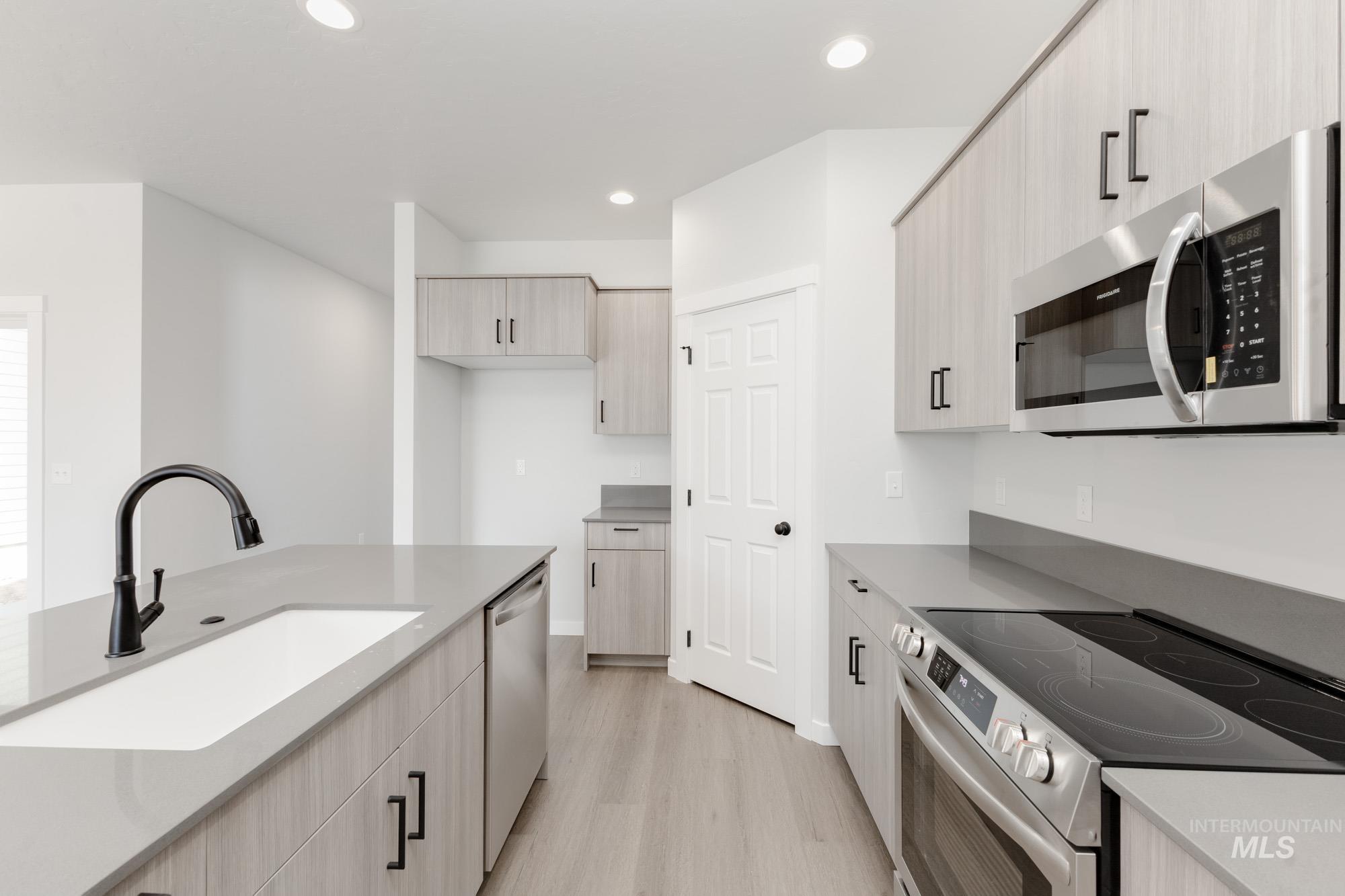 Kitchen featuring stainless steel appliances, light wood-type flooring, recessed lighting, light brown cabinetry, and light stone countertops