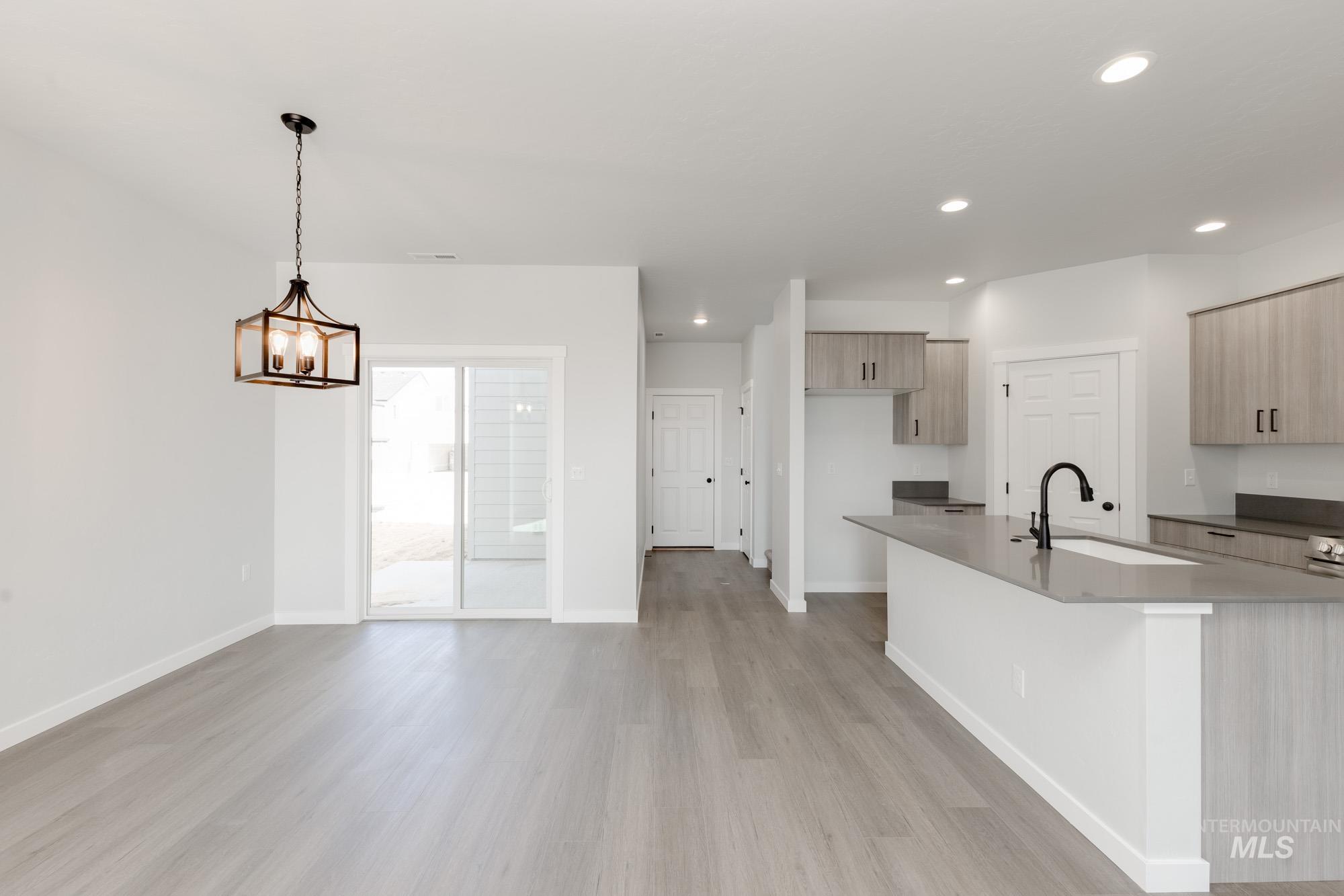 Kitchen with light wood-type flooring, recessed lighting, modern cabinets, dark stone countertops, and decorative light fixtures