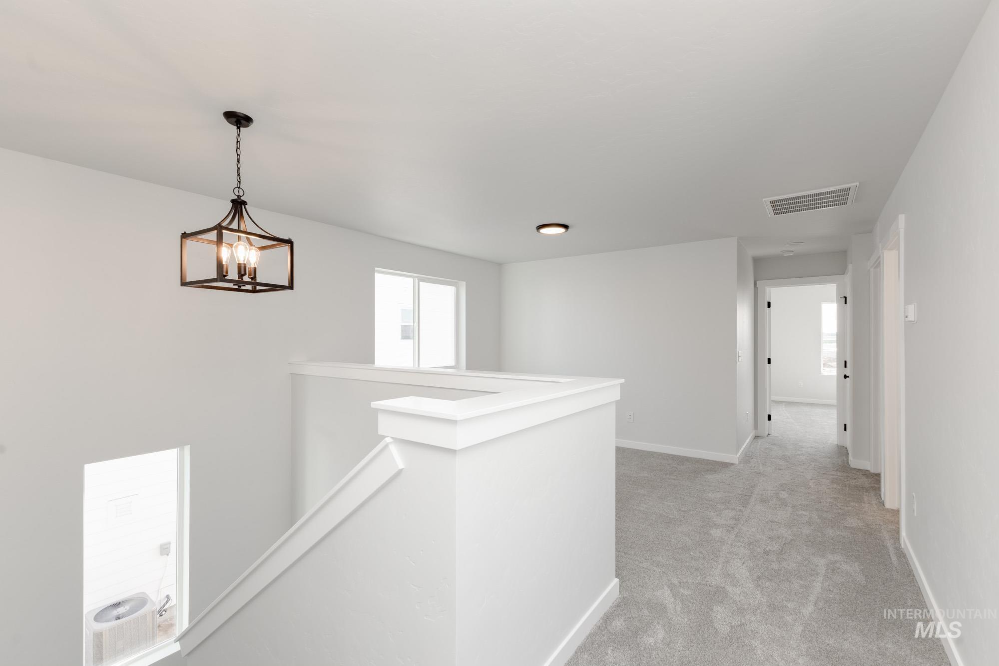 Corridor featuring an upstairs landing, light colored carpet, and a chandelier