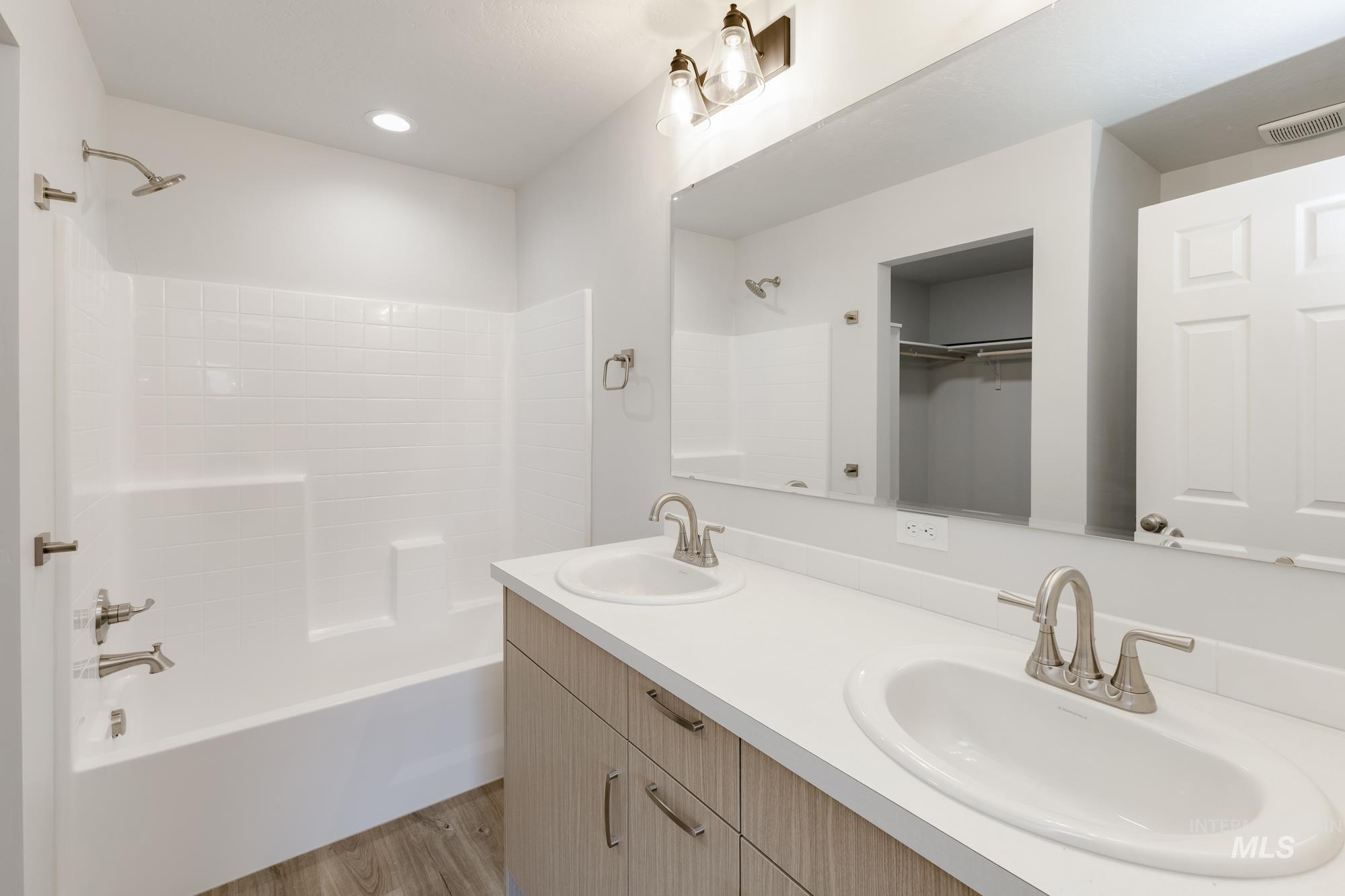 Bathroom featuring double vanity, shower / tub combination, light wood-type flooring, a walk in closet, and recessed lighting