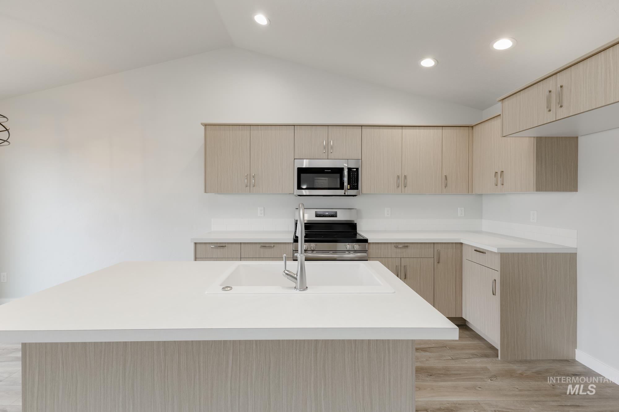 Kitchen featuring light brown cabinetry, stainless steel appliances, light wood-type flooring, vaulted ceiling, and modern cabinets