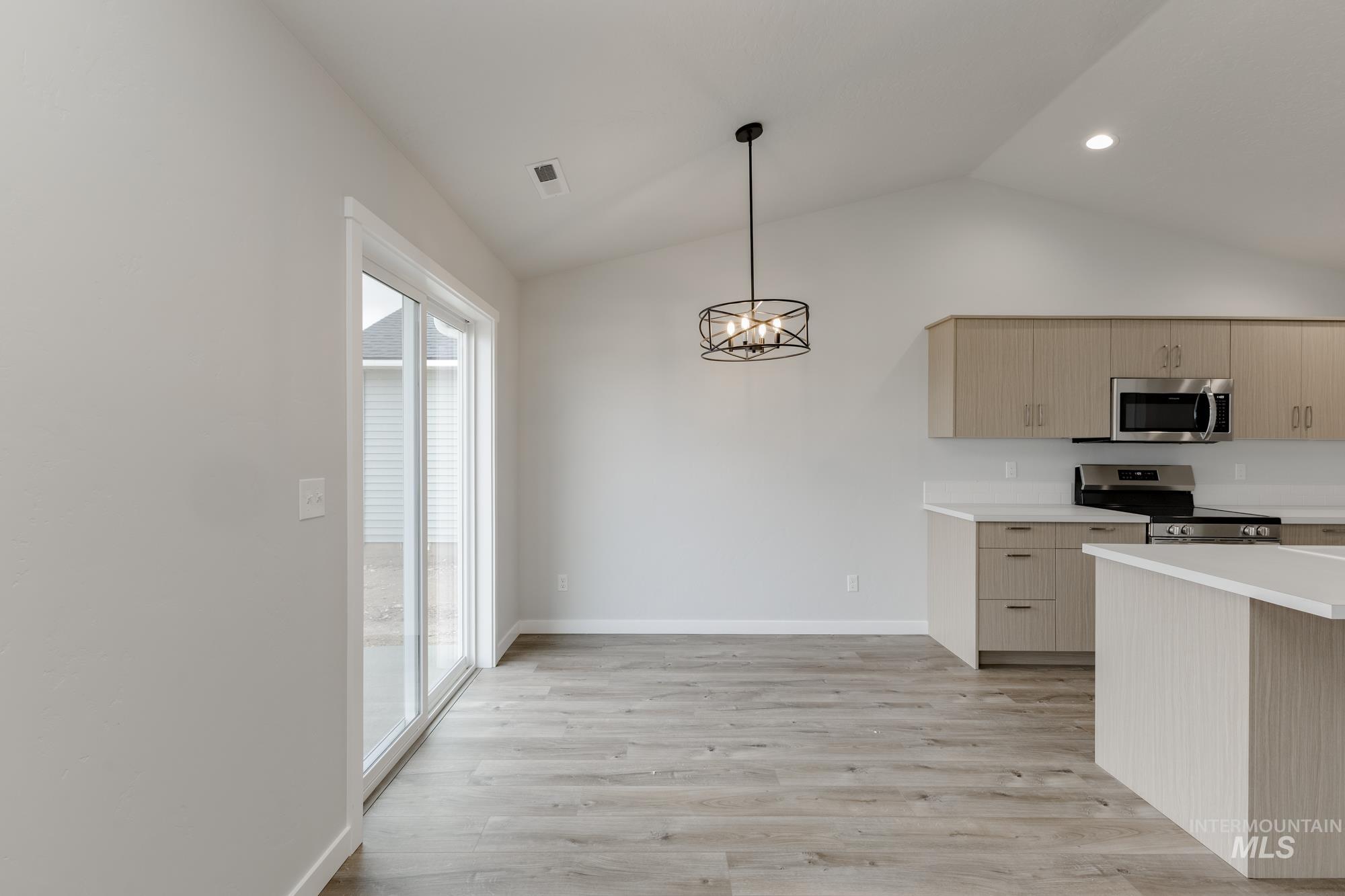 Kitchen with light countertops, a chandelier, light wood-style flooring, appliances with stainless steel finishes, and hanging light fixtures