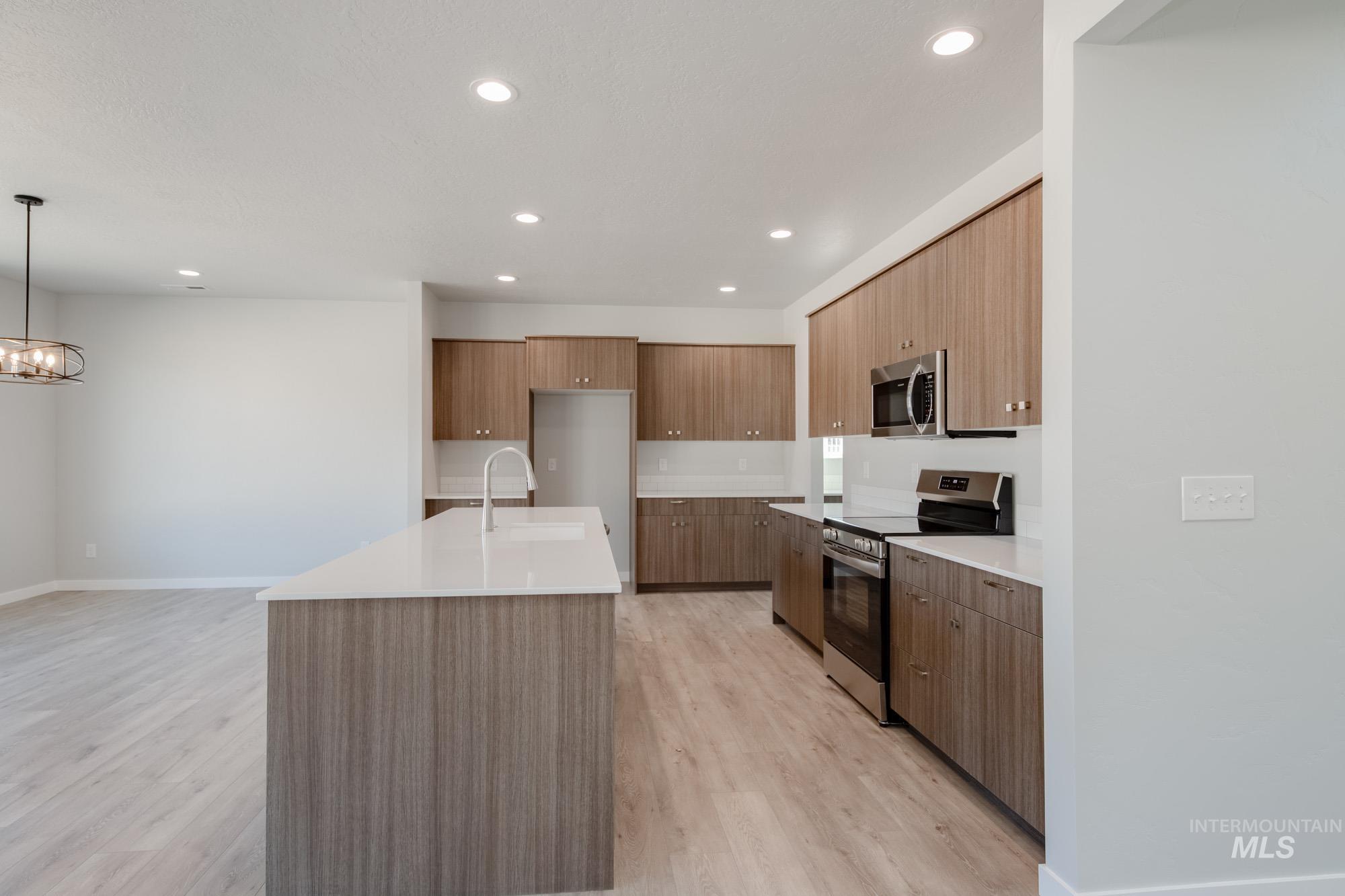 Kitchen featuring stainless steel appliances, modern cabinets, light wood-style floors, an island with sink, and decorative light fixtures