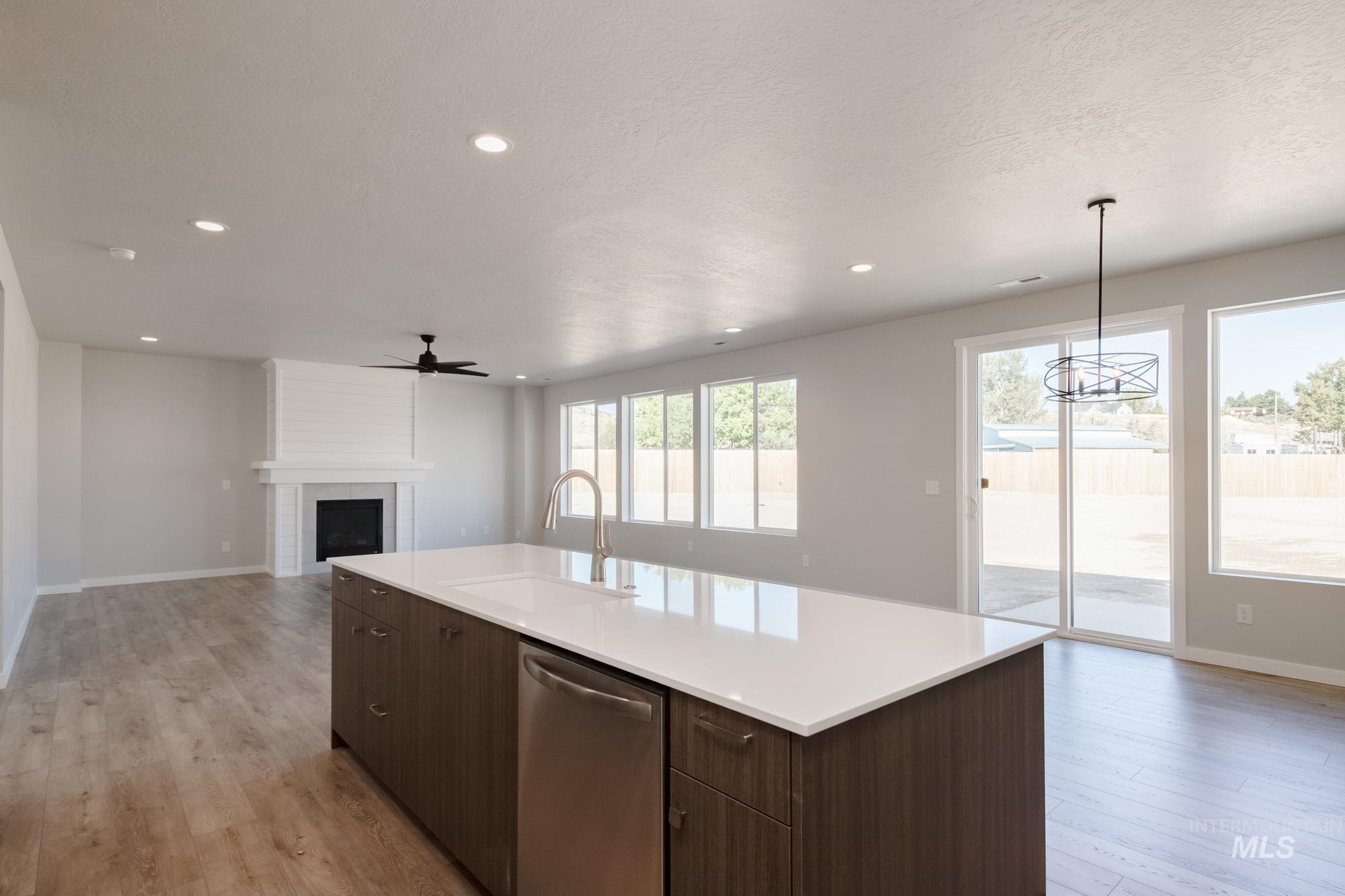 Kitchen with dark brown cabinets, open floor plan, dishwasher, a fireplace, and light wood-style flooring