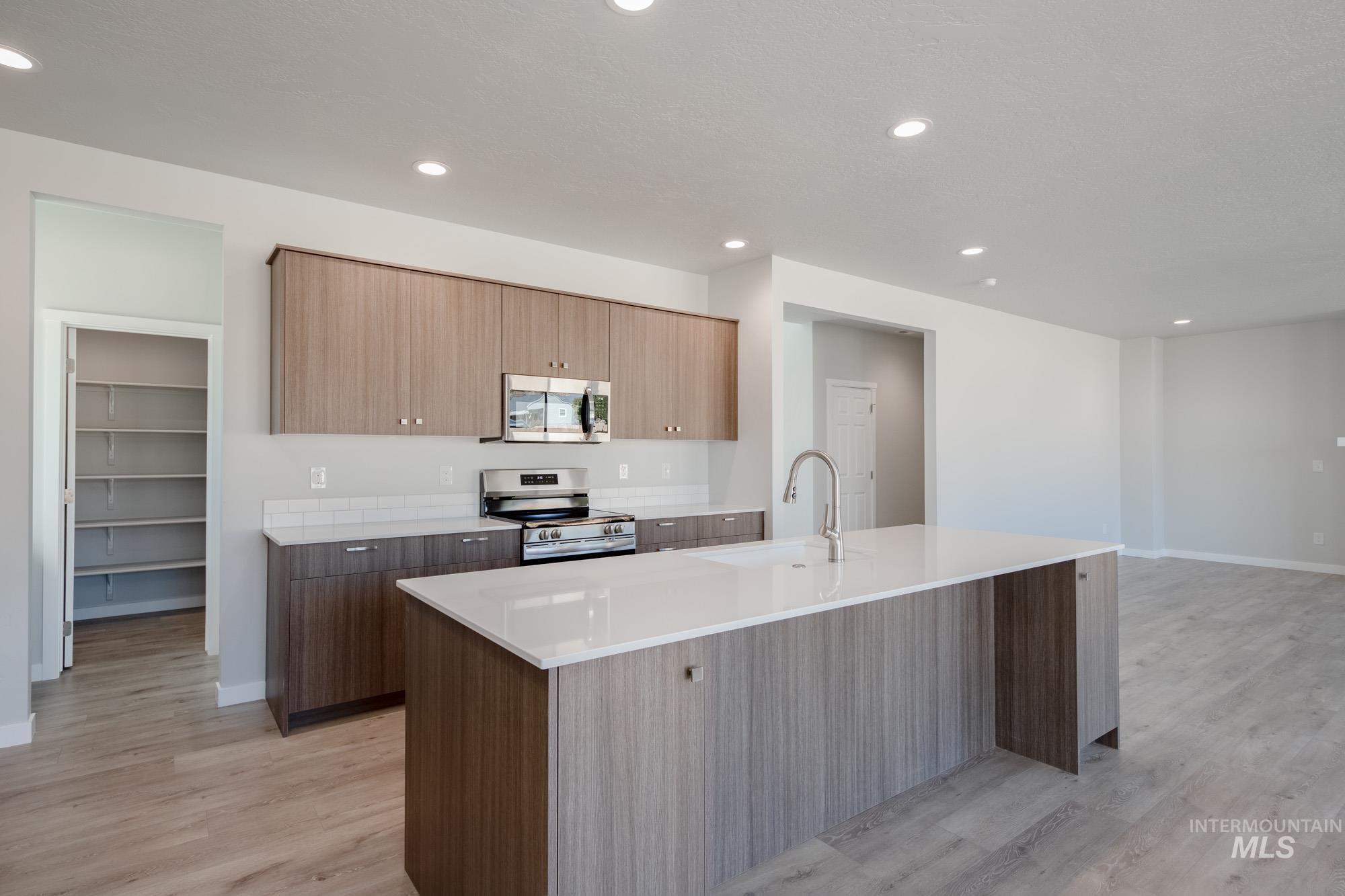 Kitchen with stainless steel appliances, recessed lighting, light stone counters, light wood-type flooring, and an island with sink