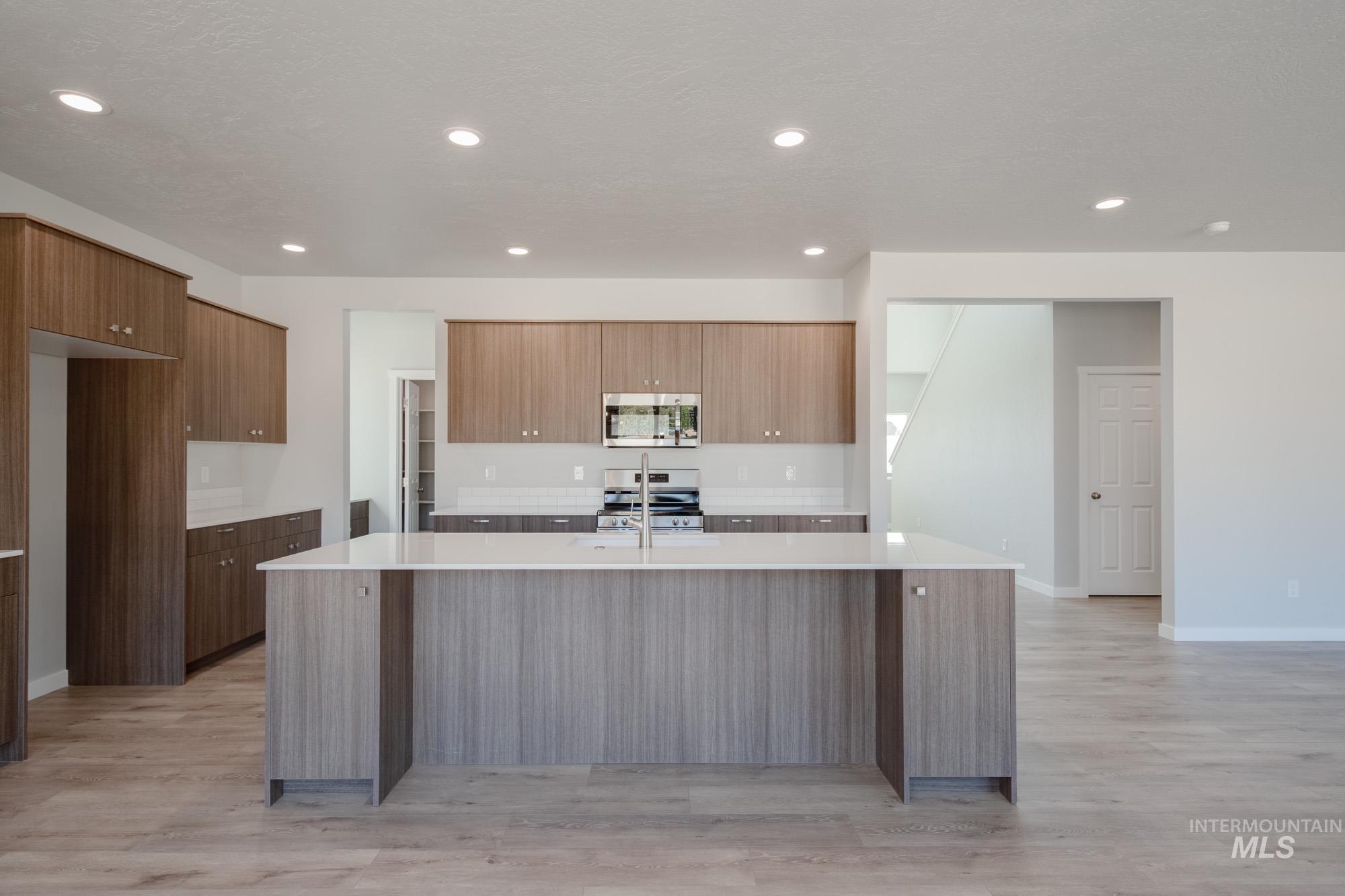Kitchen featuring modern cabinets, an island with sink, light wood finished floors, stainless steel appliances, and light stone counters