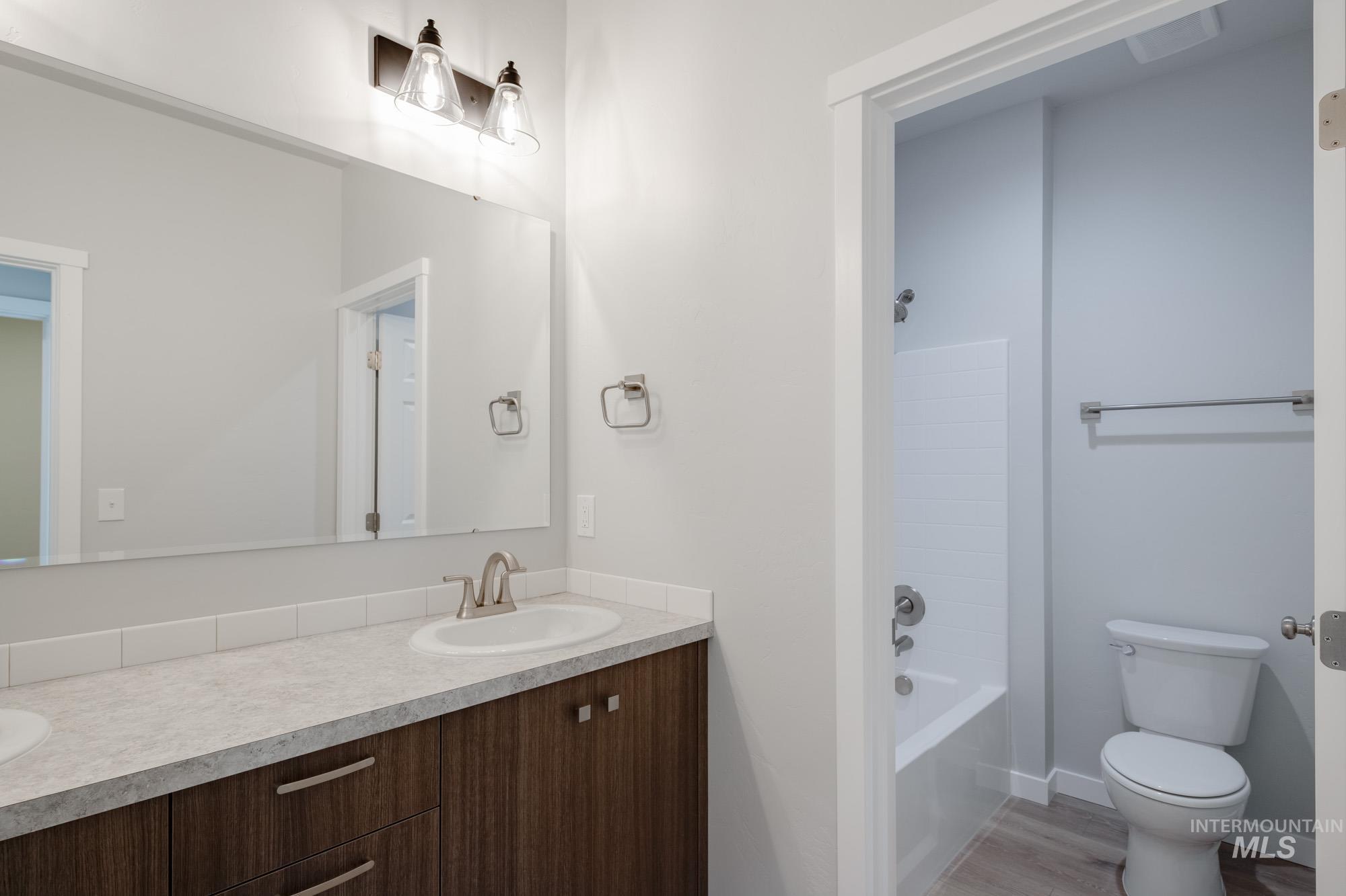Full bathroom with double vanity, shower / washtub combination, and light wood-style floors