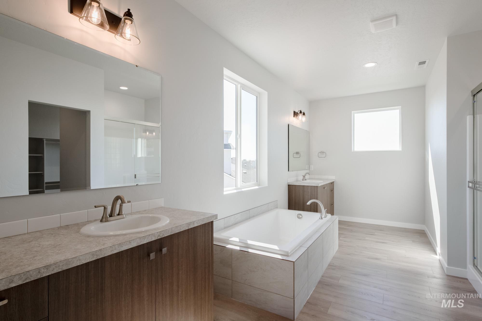 Full bath featuring a stall shower, two vanities, plenty of natural light, a garden tub, and recessed lighting