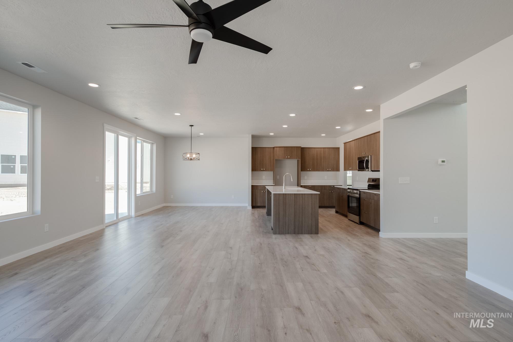 Unfurnished living room featuring a ceiling fan, recessed lighting, light wood-style floors, and a chandelier