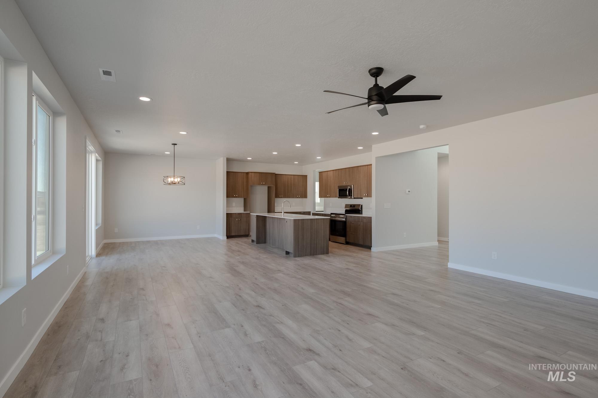 Unfurnished living room featuring recessed lighting, light wood-style floors, a ceiling fan, and a chandelier