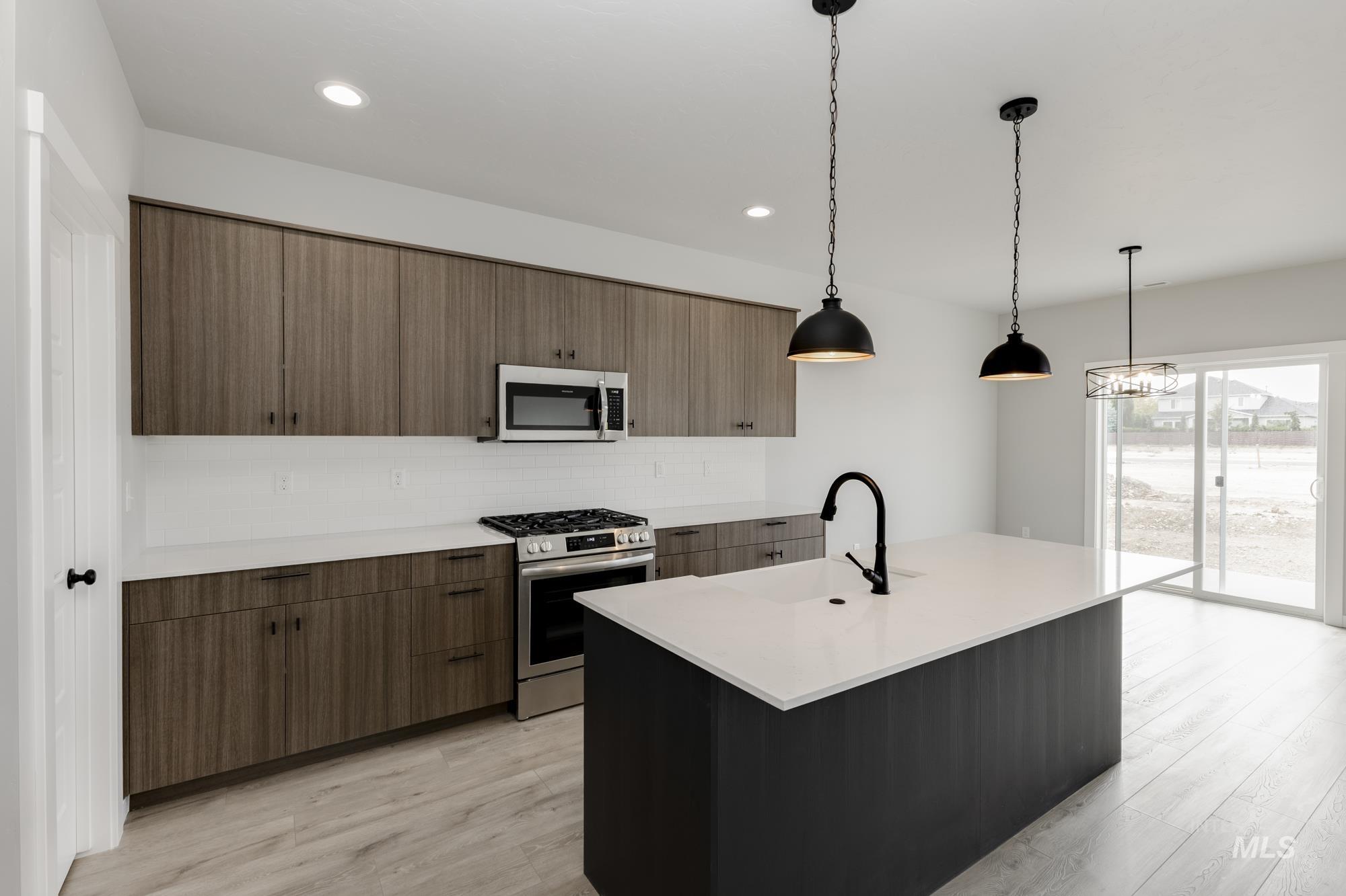 Kitchen featuring stainless steel appliances, hanging light fixtures, tasteful backsplash, a kitchen island with sink, and modern cabinets