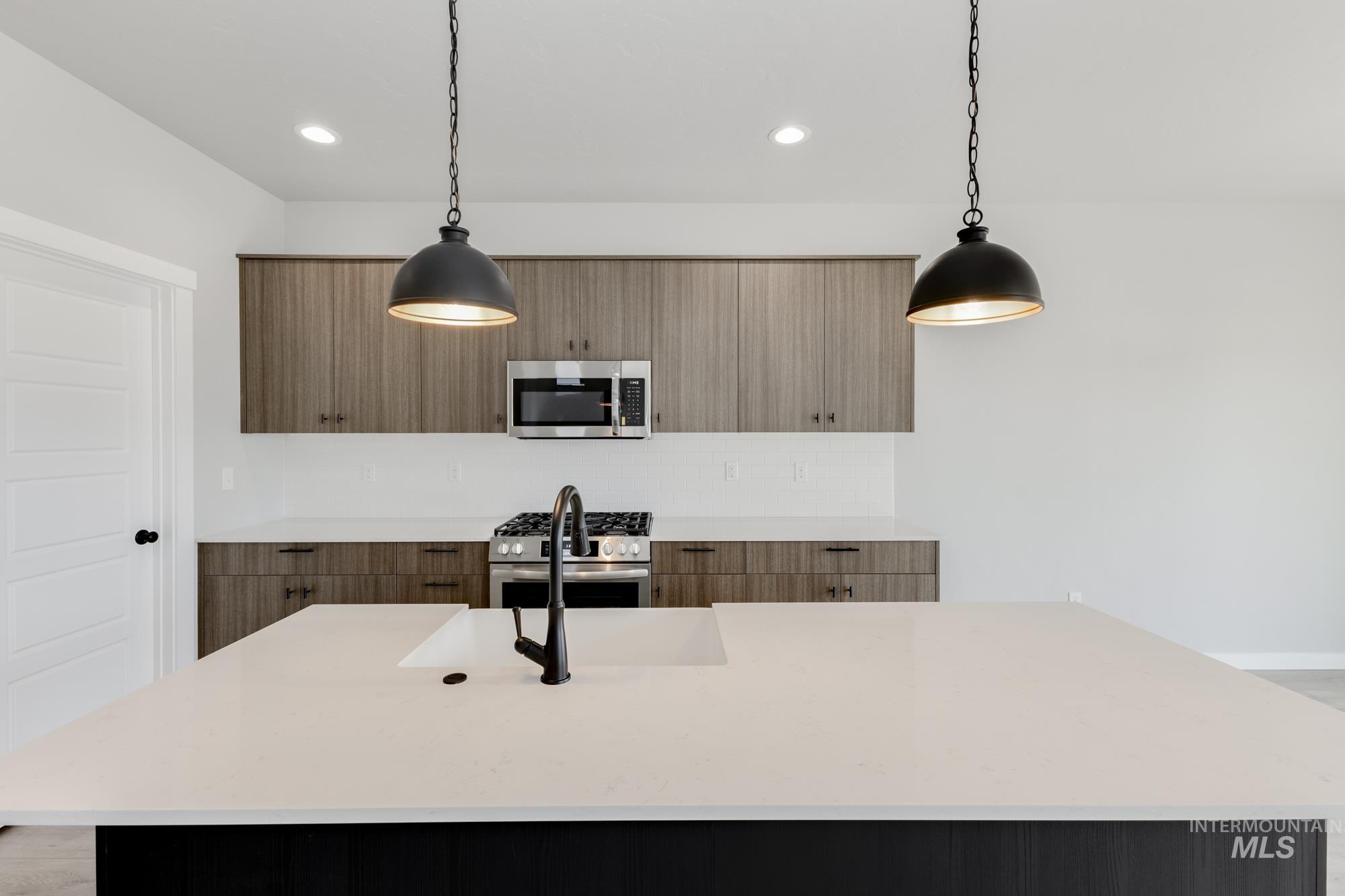 Kitchen with an island with sink, light stone counters, decorative light fixtures, stainless steel appliances, and recessed lighting
