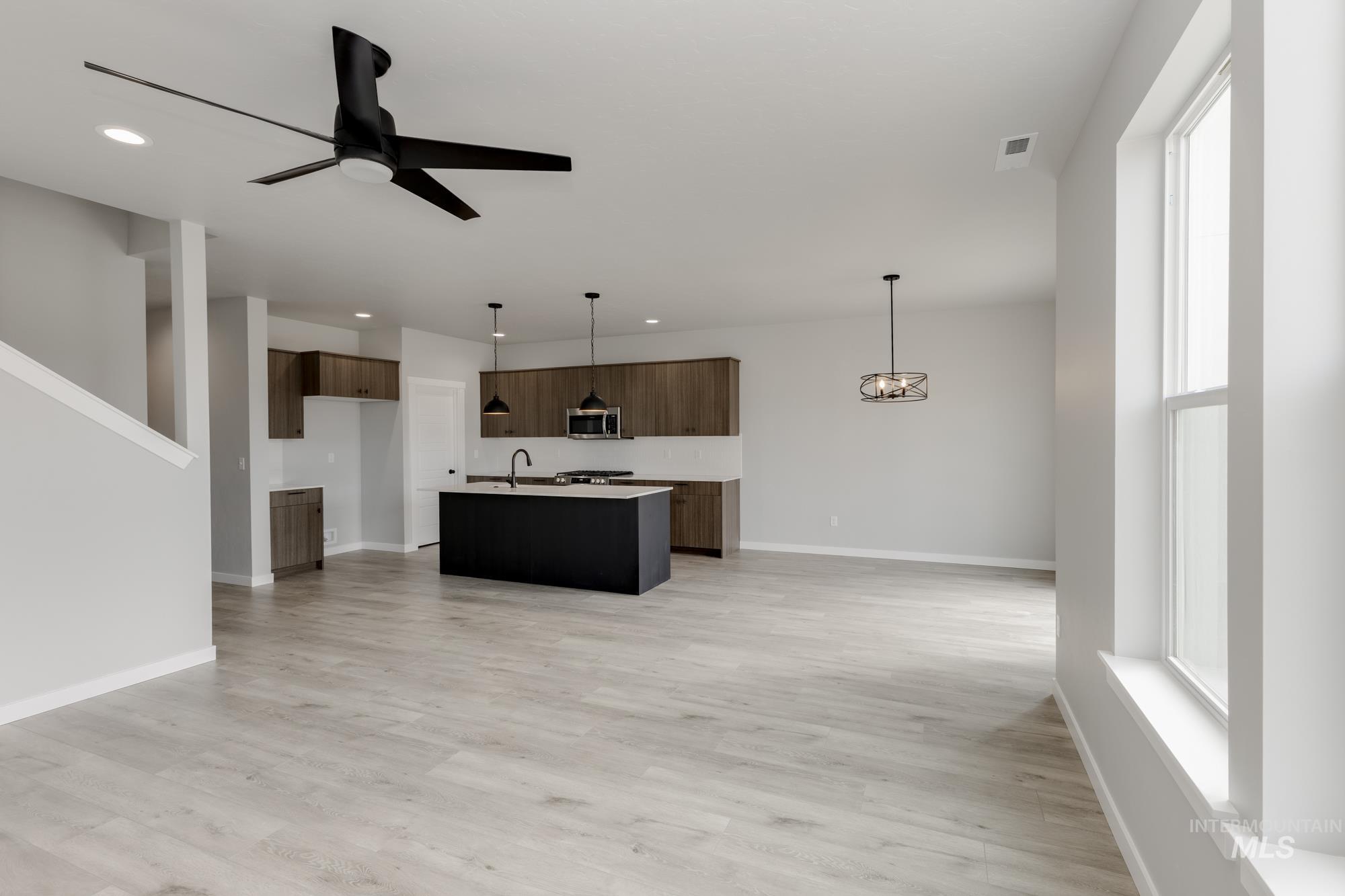 Kitchen featuring open floor plan, a kitchen island with sink, light countertops, modern cabinets, and decorative light fixtures
