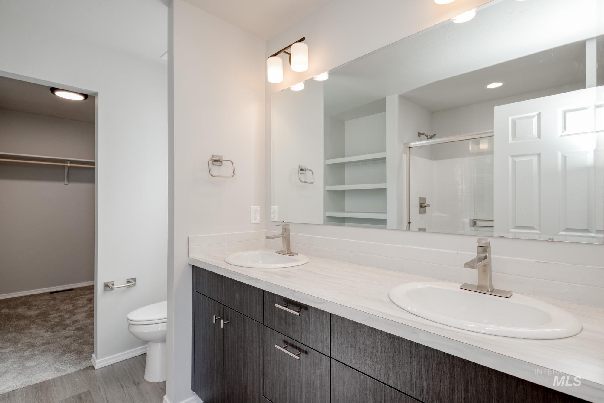 Bathroom with a spacious closet, double vanity, a stall shower, light wood-style floors, and recessed lighting