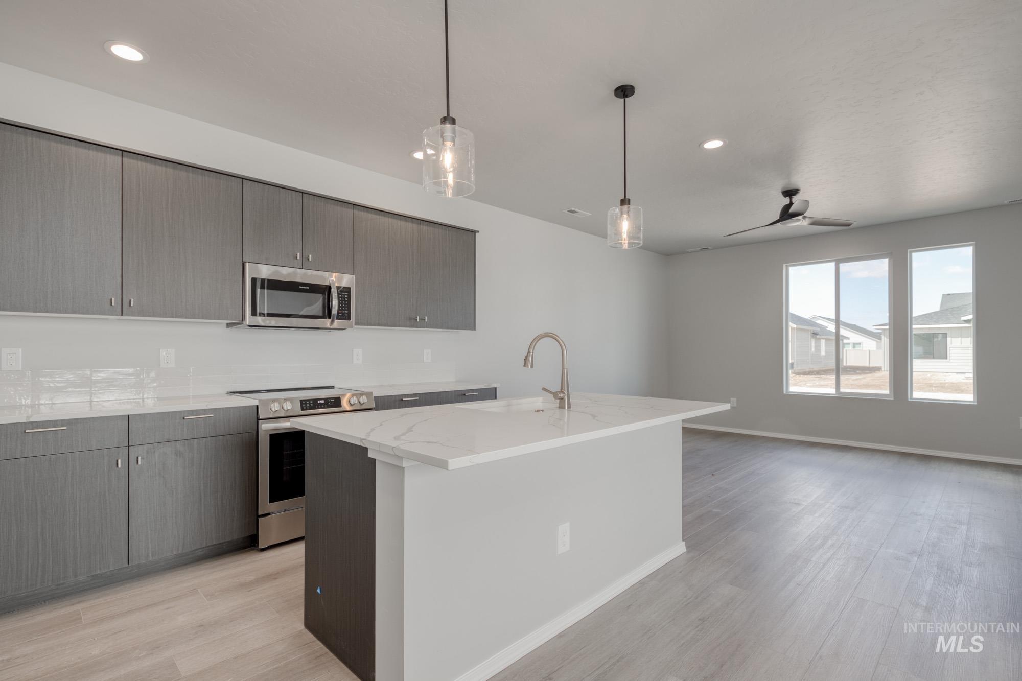 Kitchen with appliances with stainless steel finishes, pendant lighting, light stone counters, an island with sink, and modern cabinets