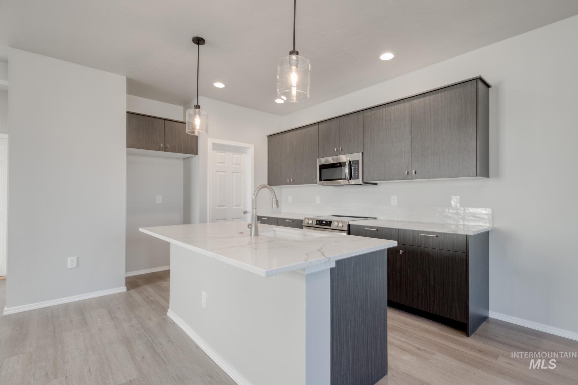 Kitchen featuring hanging light fixtures, modern cabinets, light stone counters, stainless steel appliances, and light wood-style flooring