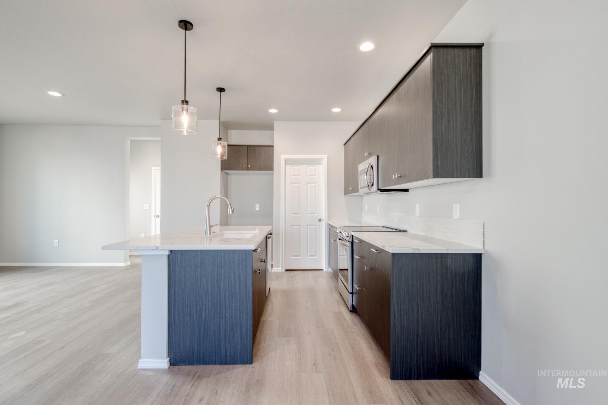 Kitchen featuring modern cabinets, stainless steel appliances, light stone countertops, a center island with sink, and recessed lighting