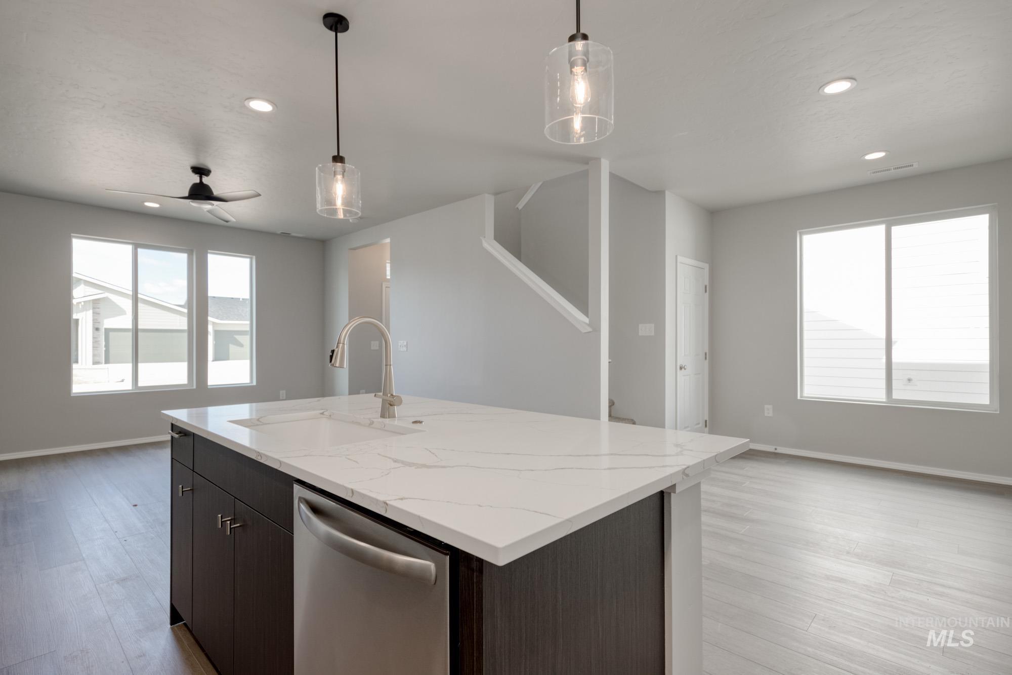 Kitchen featuring open floor plan, decorative light fixtures, dishwasher, a ceiling fan, and light stone countertops