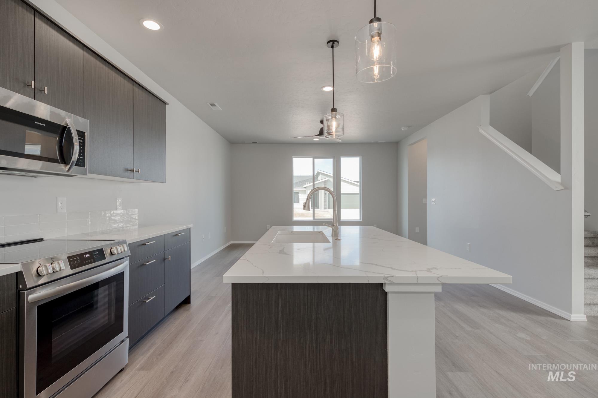 Kitchen with appliances with stainless steel finishes, an island with sink, light wood-style flooring, pendant lighting, and light stone counters