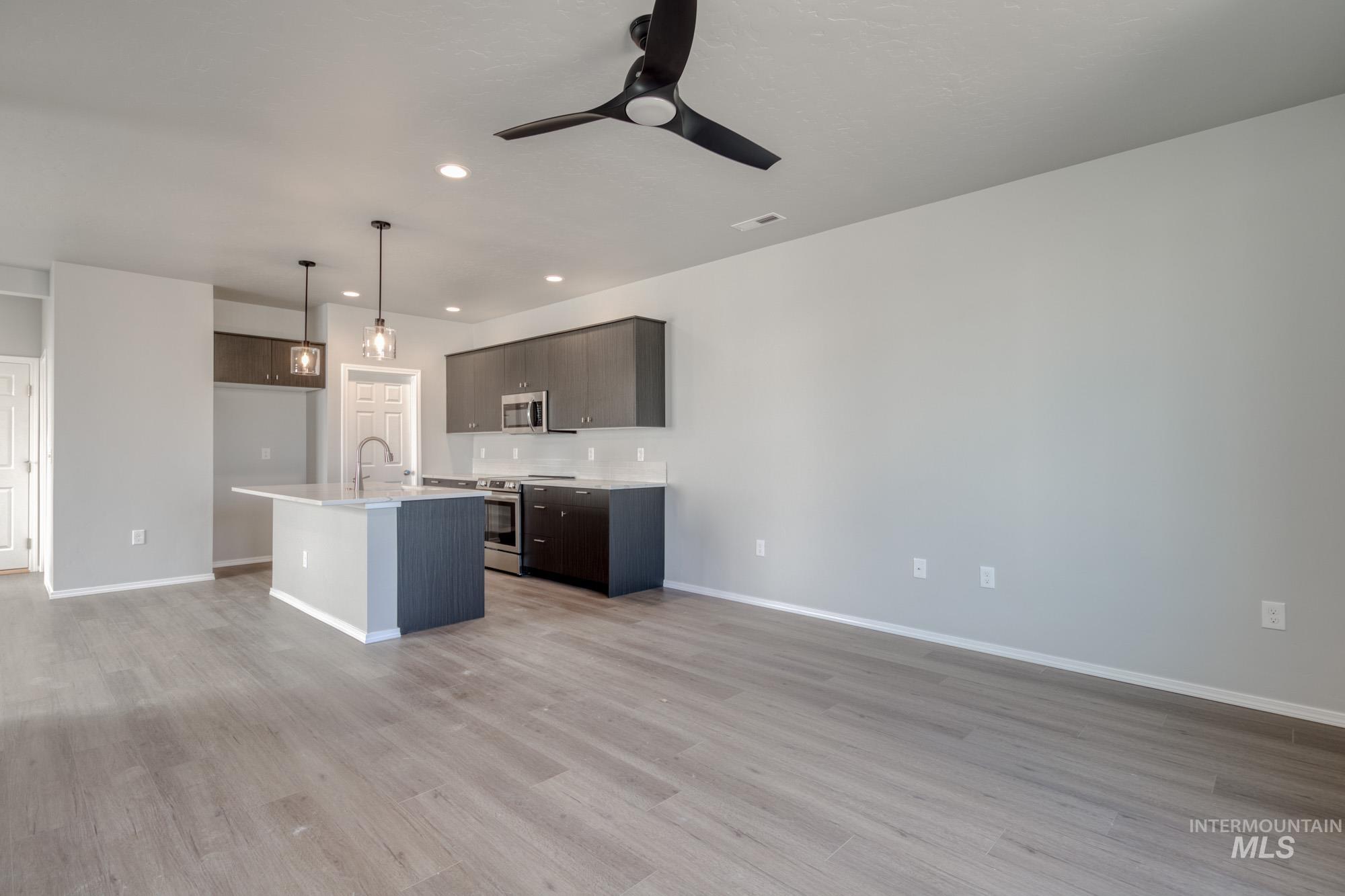 Kitchen with stainless steel appliances, an island with sink, decorative light fixtures, recessed lighting, and light wood finished floors