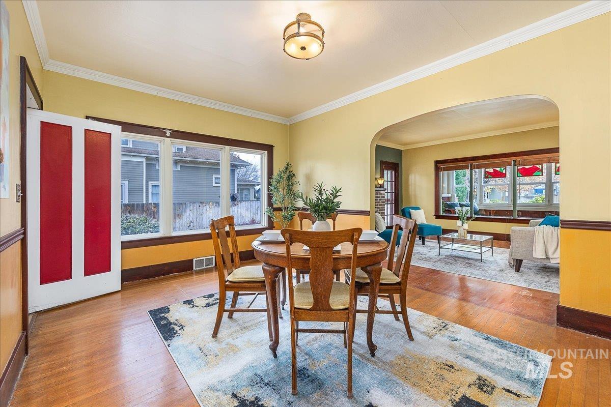 Dining area with arched walkways, light wood-style flooring, and crown molding