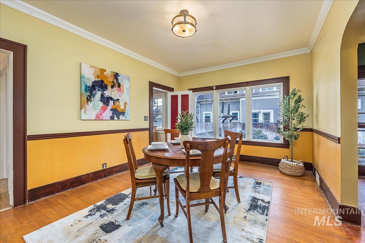 Dining area with wood-type flooring, arched walkways, and ornamental molding