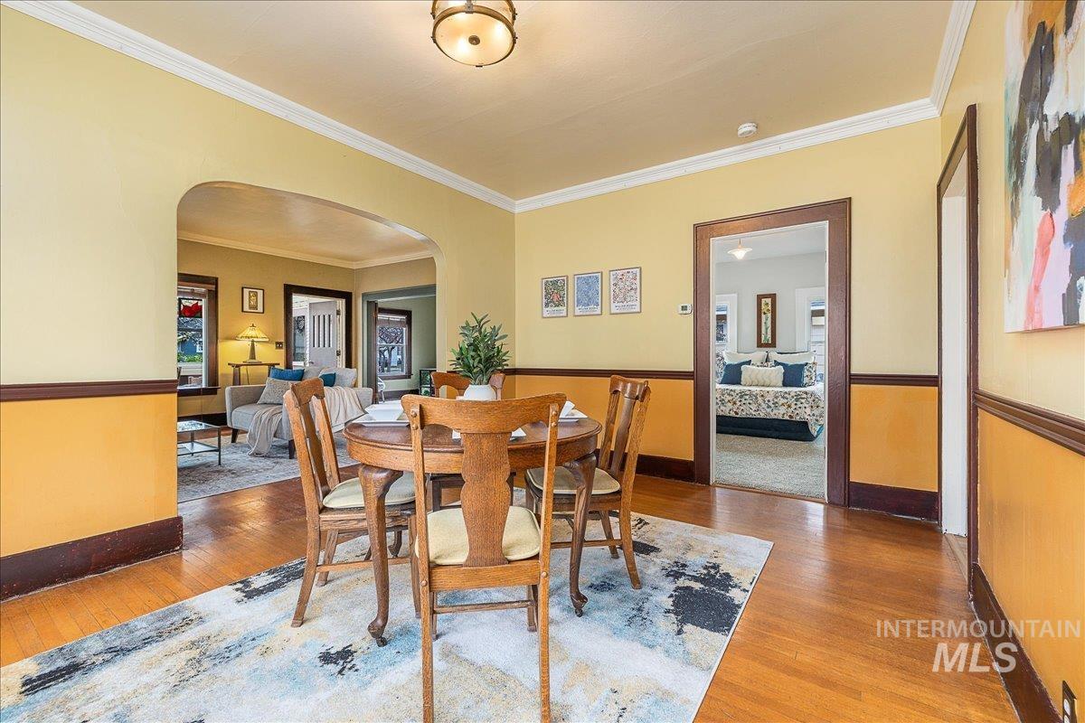 Dining room with arched walkways, wood-type flooring, and ornamental molding