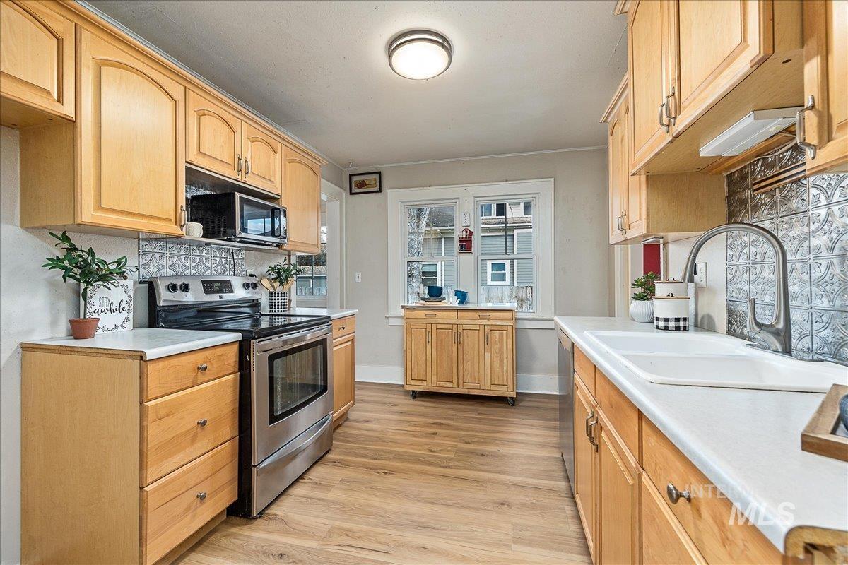 Kitchen with appliances with stainless steel finishes, light countertops, light wood-style flooring, and decorative backsplash