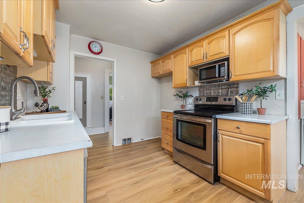 Kitchen featuring stainless steel electric range oven, light countertops, backsplash, light wood-style floors, and crown molding