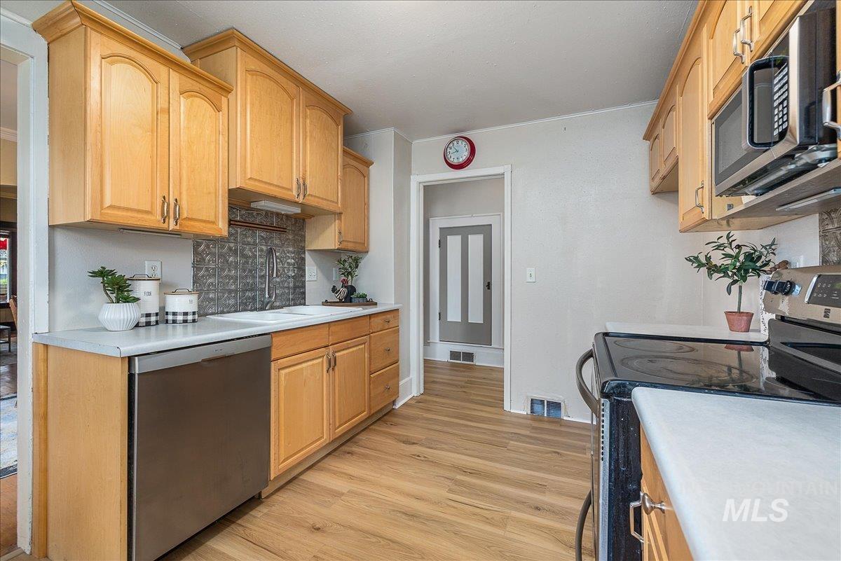 Kitchen with stainless steel appliances, light countertops, light wood-type flooring, decorative backsplash, and crown molding