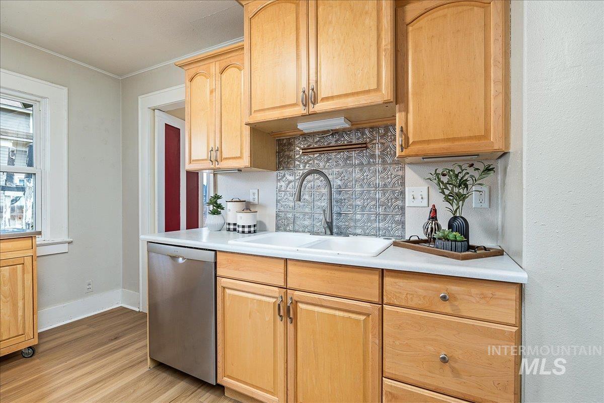 Kitchen with light countertops, light brown cabinets, stainless steel dishwasher, backsplash, and light wood-style flooring