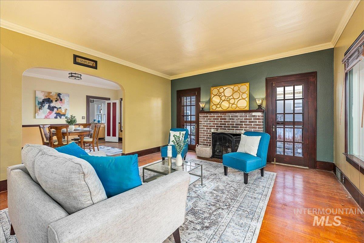 Living room with a fireplace, crown molding, wood finished floors, and arched walkways