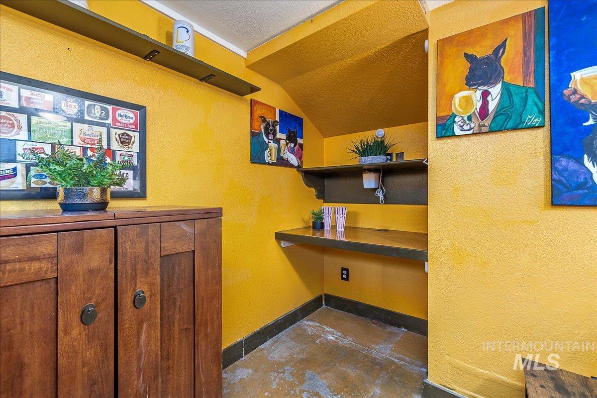 Bar area with lofted ceiling, a textured wall, and concrete floors