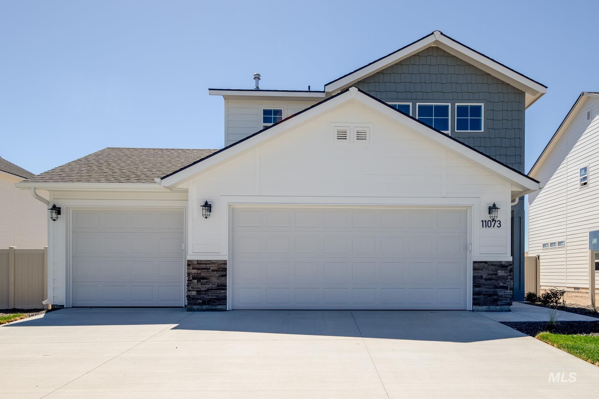 View of front facade with stone siding, driveway, a garage, and a shingled roof