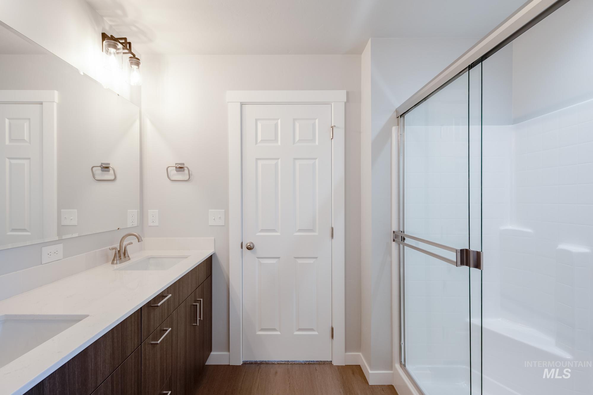 Bathroom with light wood-style flooring, double vanity, and a shower stall