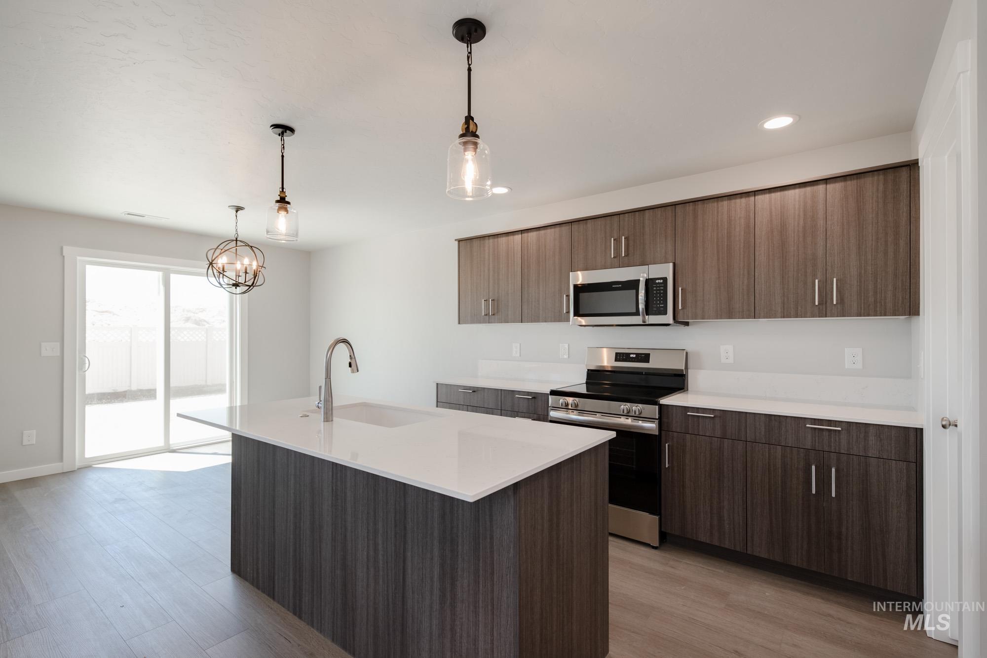 Kitchen with stainless steel appliances, decorative light fixtures, a kitchen island with sink, light wood-type flooring, and recessed lighting