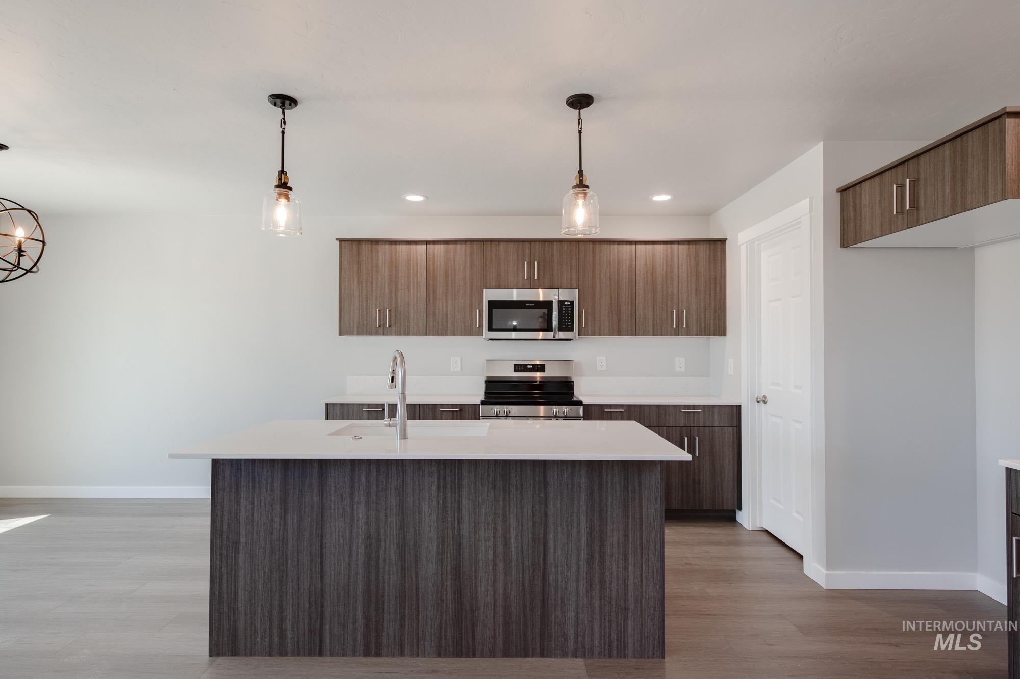 Kitchen featuring pendant lighting, modern cabinets, stainless steel appliances, a kitchen island with sink, and light wood-style floors