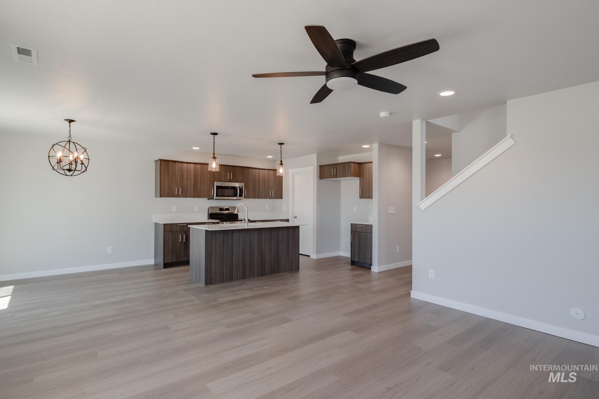 Kitchen featuring open floor plan, decorative light fixtures, a center island with sink, light wood-style flooring, and appliances with stainless steel finishes