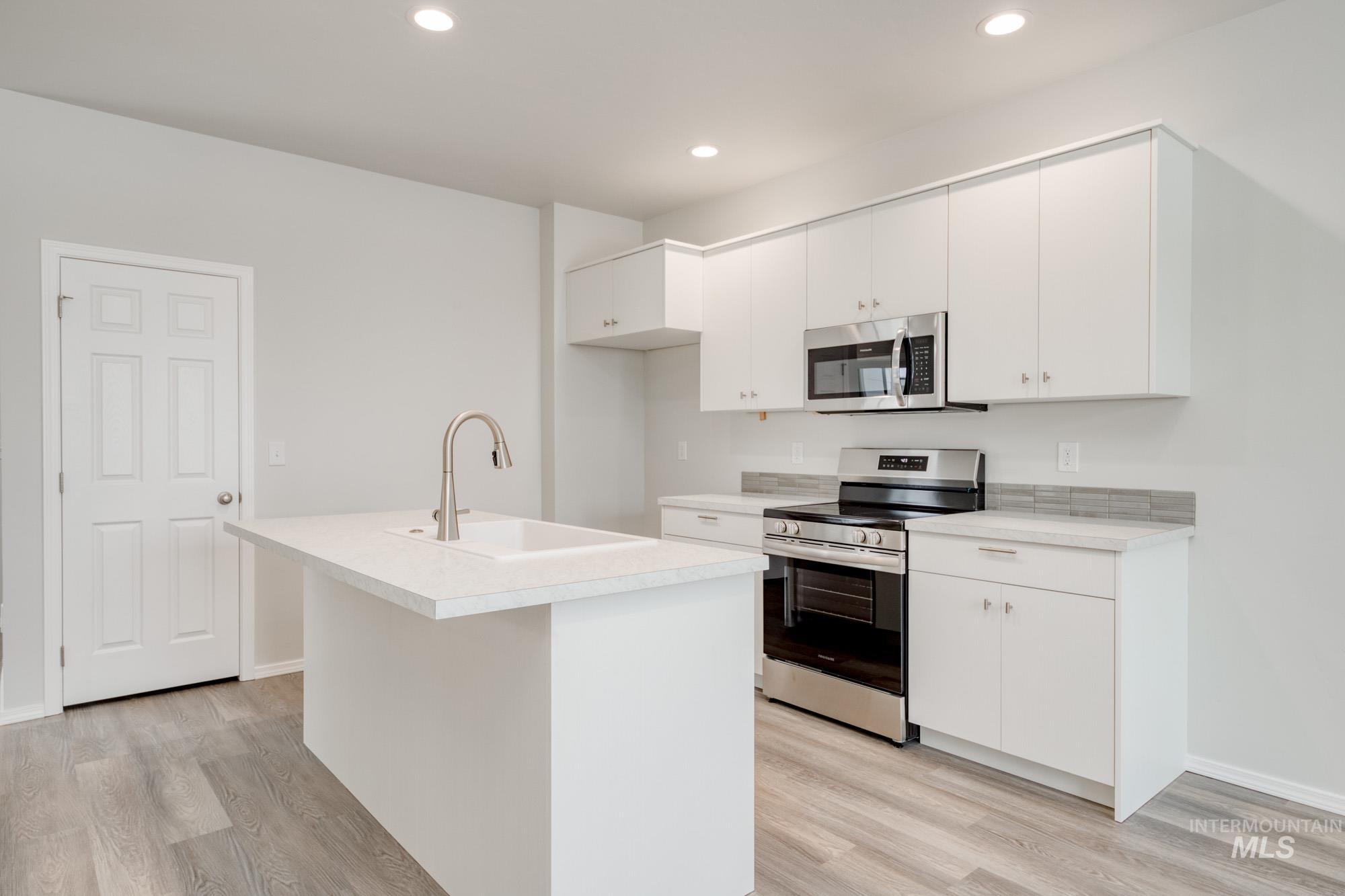 Kitchen featuring stainless steel appliances, light countertops, white cabinets, light wood finished floors, and recessed lighting